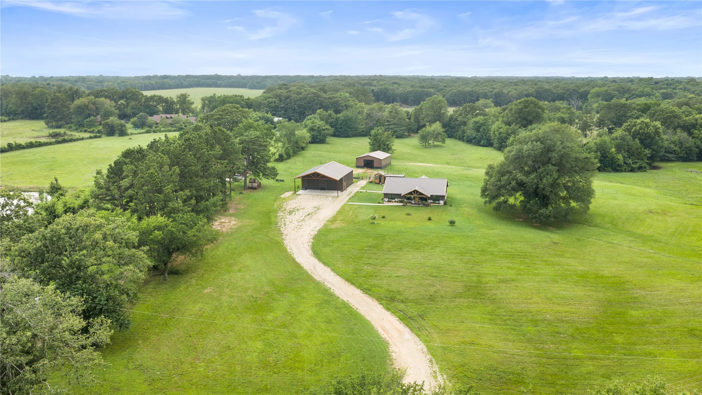 Expansive green acreage featuring a main residence with a covered porch, a large barn structure, a secondary shed, and a winding gravel driveway