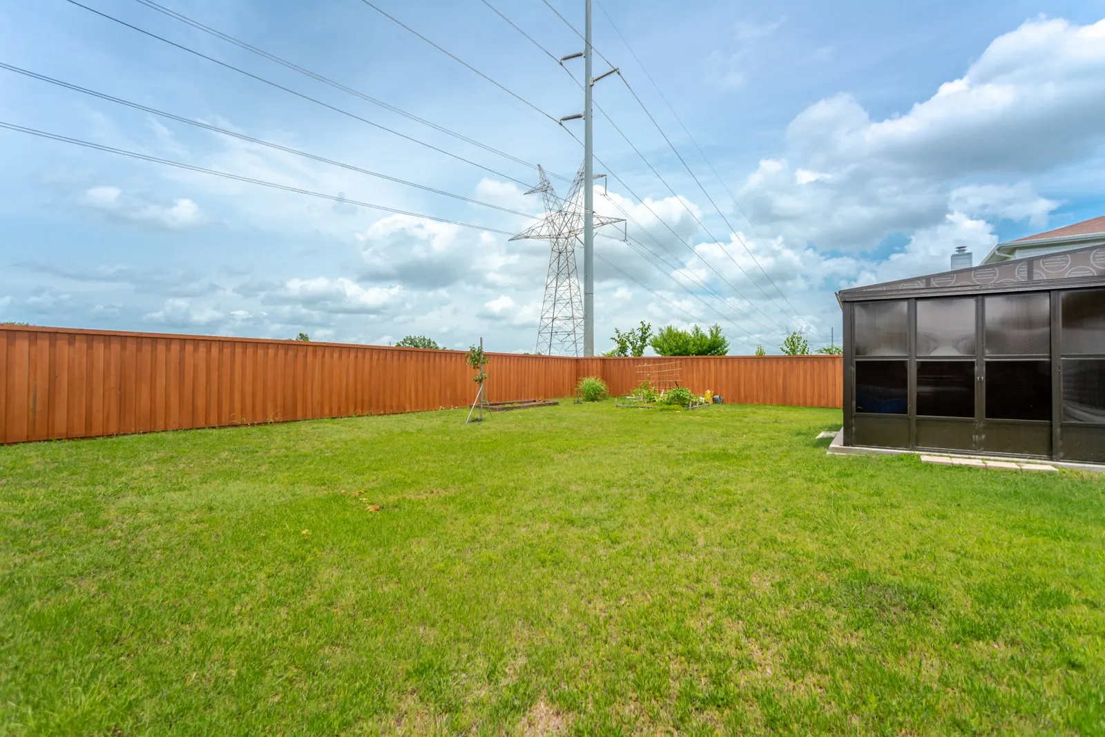 Expansive backyard featuring a green lawn, wood privacy fencing, and a built-in sunroom structure with dark-tinted panels