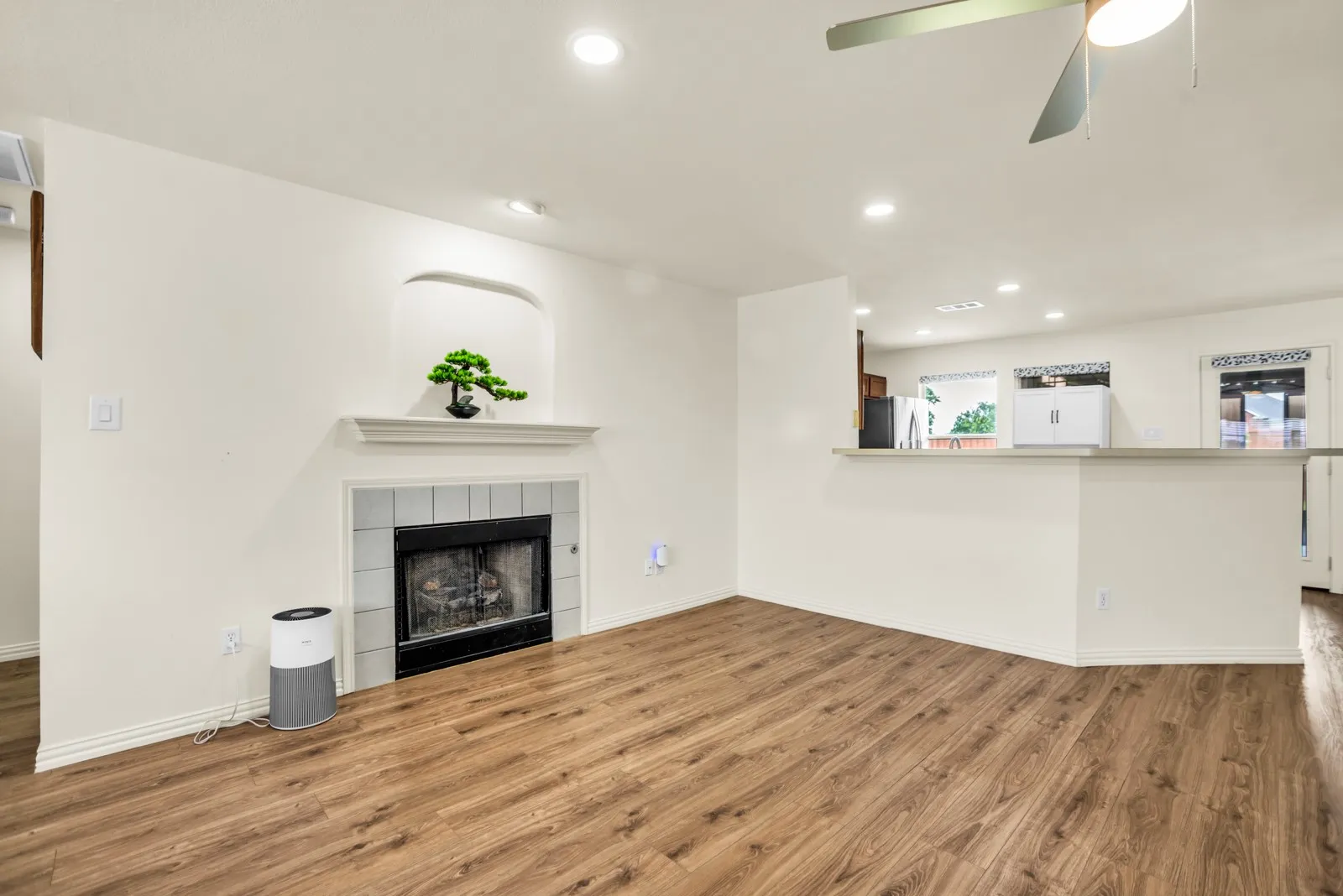 Living area with wood-finish flooring, a fireplace with a light-colored tile surround, and a mantel with an arched niche above