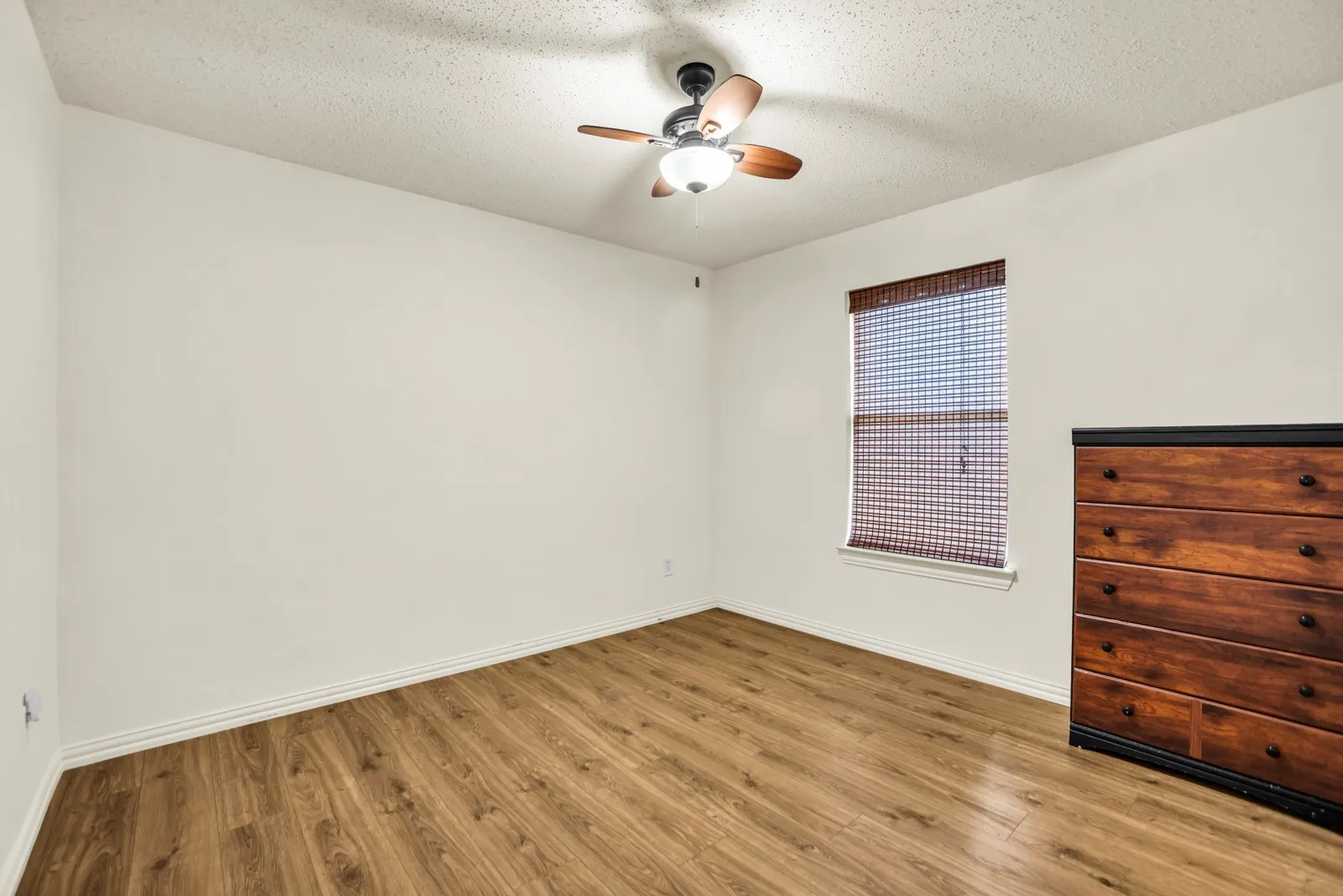 Room featuring wood-finish flooring, white baseboards, and a ceiling fan with light fixture