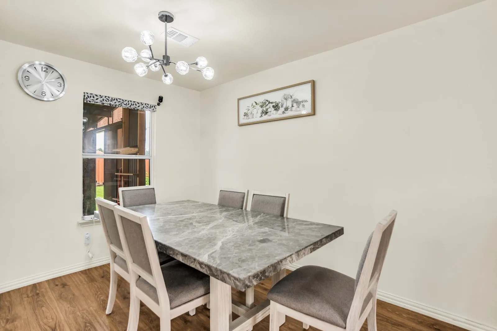 Dining space featuring wood-finish flooring, a modern chandelier, and a window with a patterned valance