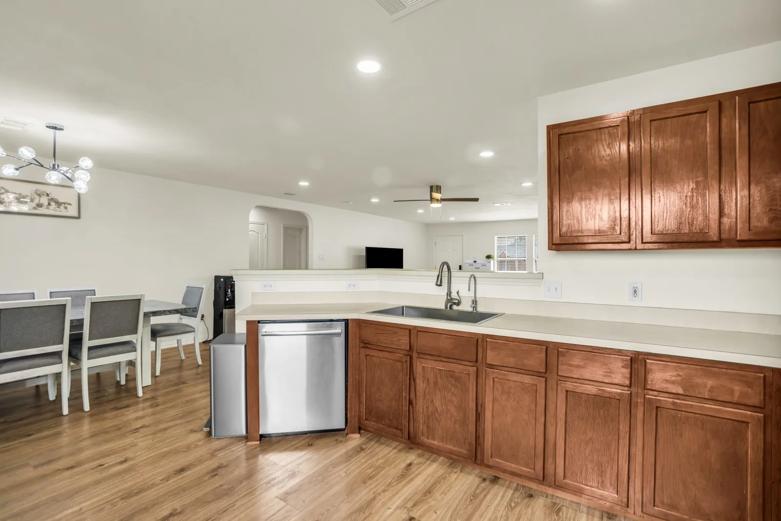 Kitchen featuring wood-finish flooring, undermount stainless steel sink with gooseneck faucet, light-toned countertops, wood cabinetry, and a stainless steel dishwasher