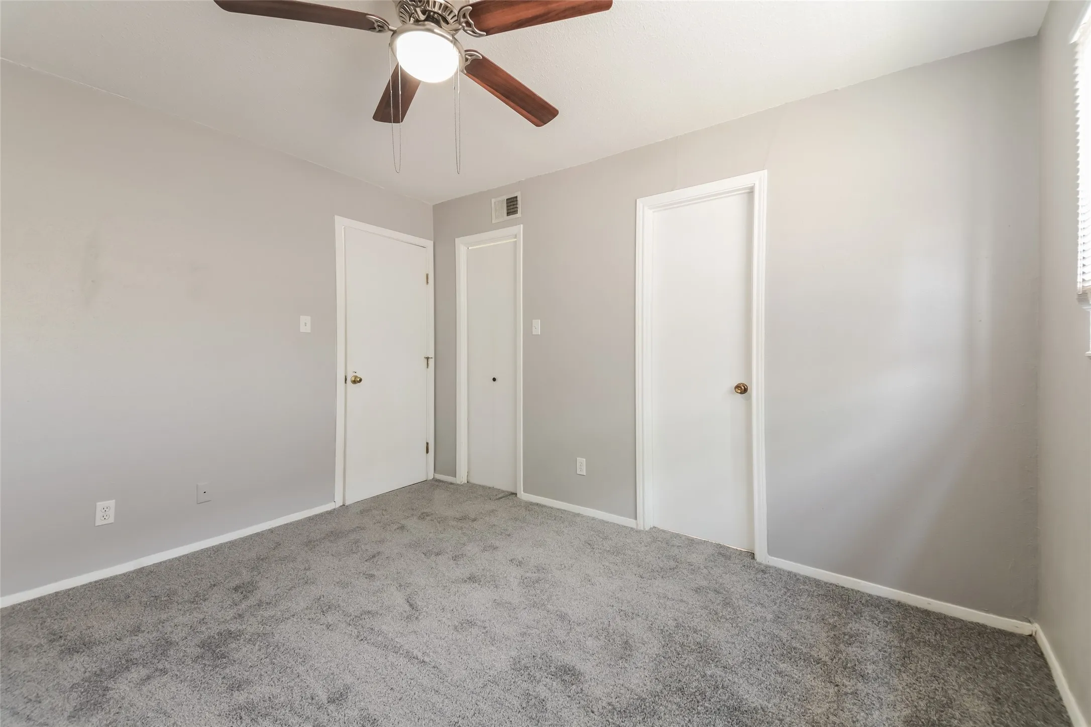 Carpeted room featuring light gray walls, a ceiling fan with wood-finish blades, and white interior doors with brass-finish hardware
