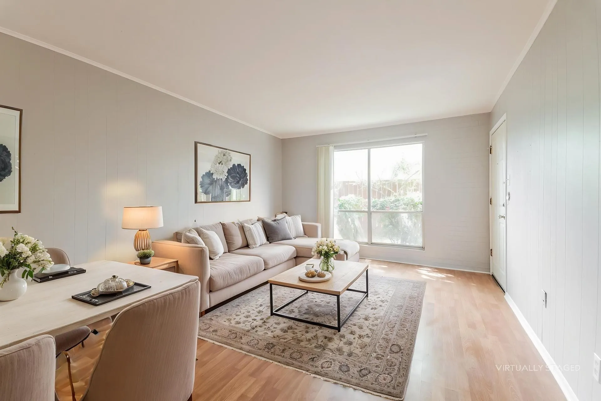 Open-concept living area featuring light-toned wood-finish flooring, a large window, and neutral wall tones