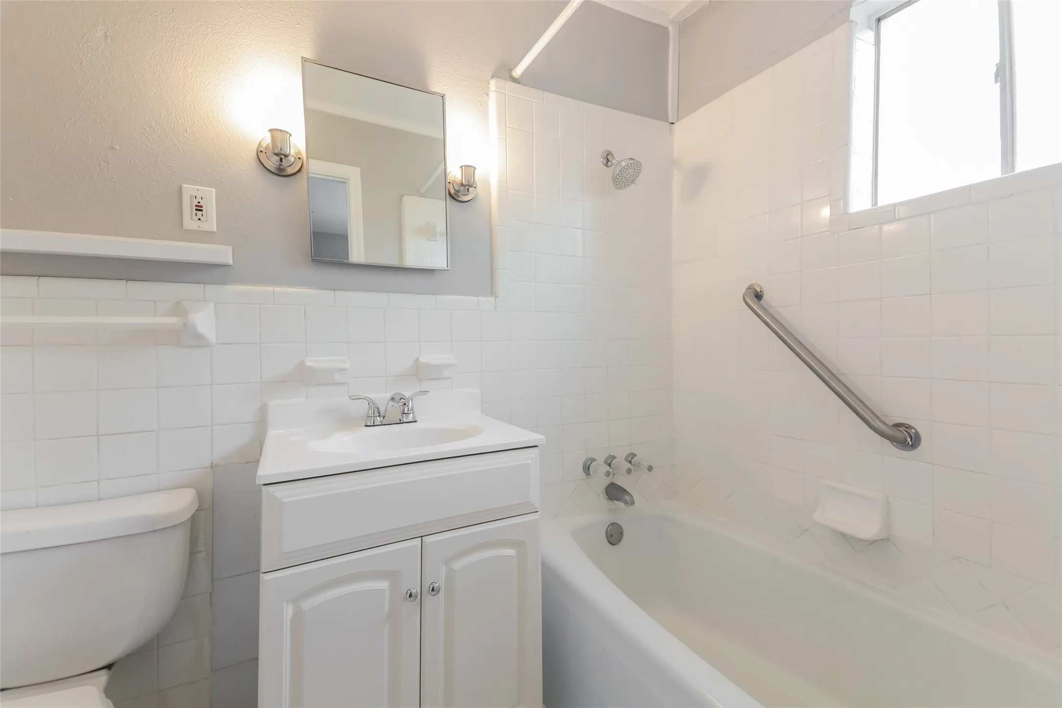 Bathroom featuring a white vanity with cabinet storage, chrome faucet, and rectangular mirror with sconce lighting