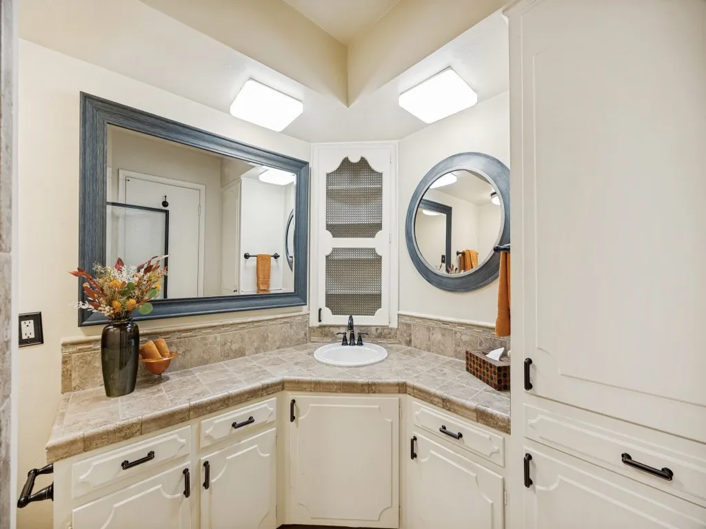 Ensuite bathroom features ample cabinetry, fresh paint, tiled countertop, and retro medicine cabinet.