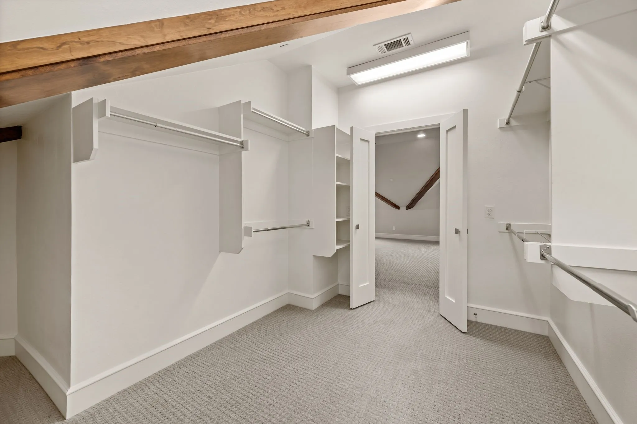 Expansive walk-in closet featuring white built-in shelving, chrome hanging rods, a textured carpet floor, and overhead fluorescent lighting