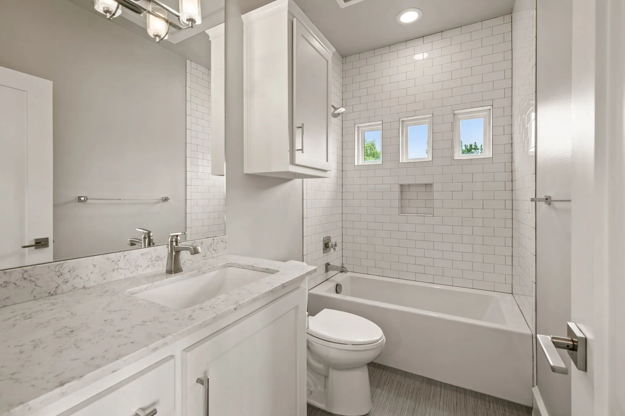 Bathroom featuring a white subway tile surround, three transom windows, and a built-in shower niche