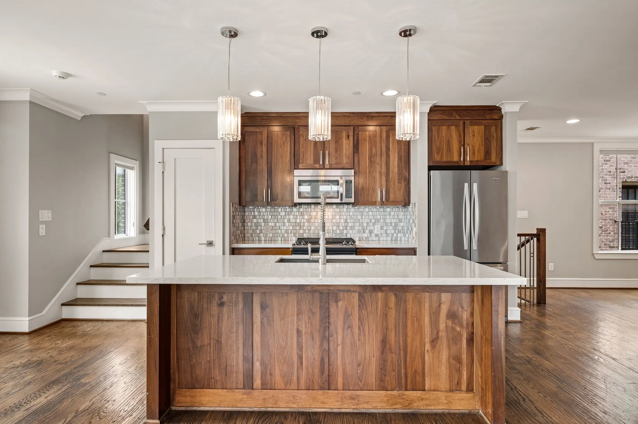 Kitchen island with a light-toned countertop, wood-finish cabinetry, stainless steel appliances, a mosaic tile backsplash, and wood-finish flooring