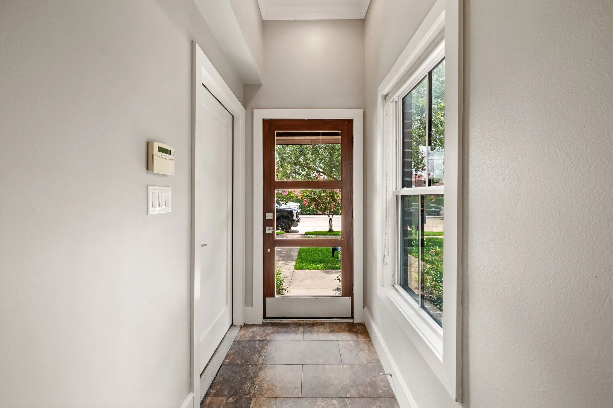 Foyer featuring a wood-finish entry door with clear glass panels, an adjacent double-hung window, white trim throughout, textured light gray walls, and large format tile flooring