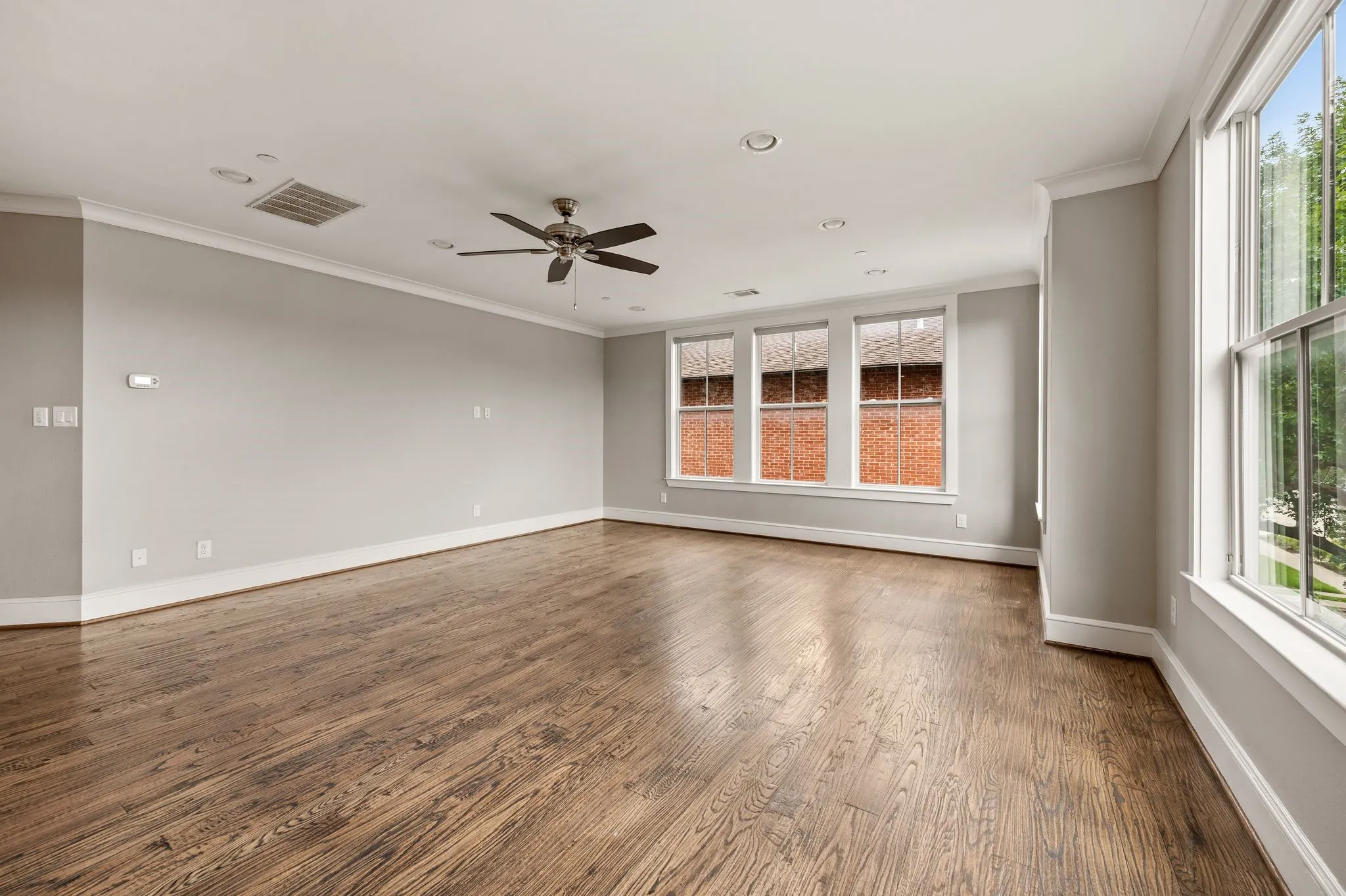 Spacious room featuring wood-finish flooring, tall windows, recessed lighting, crown molding, and a ceiling fan