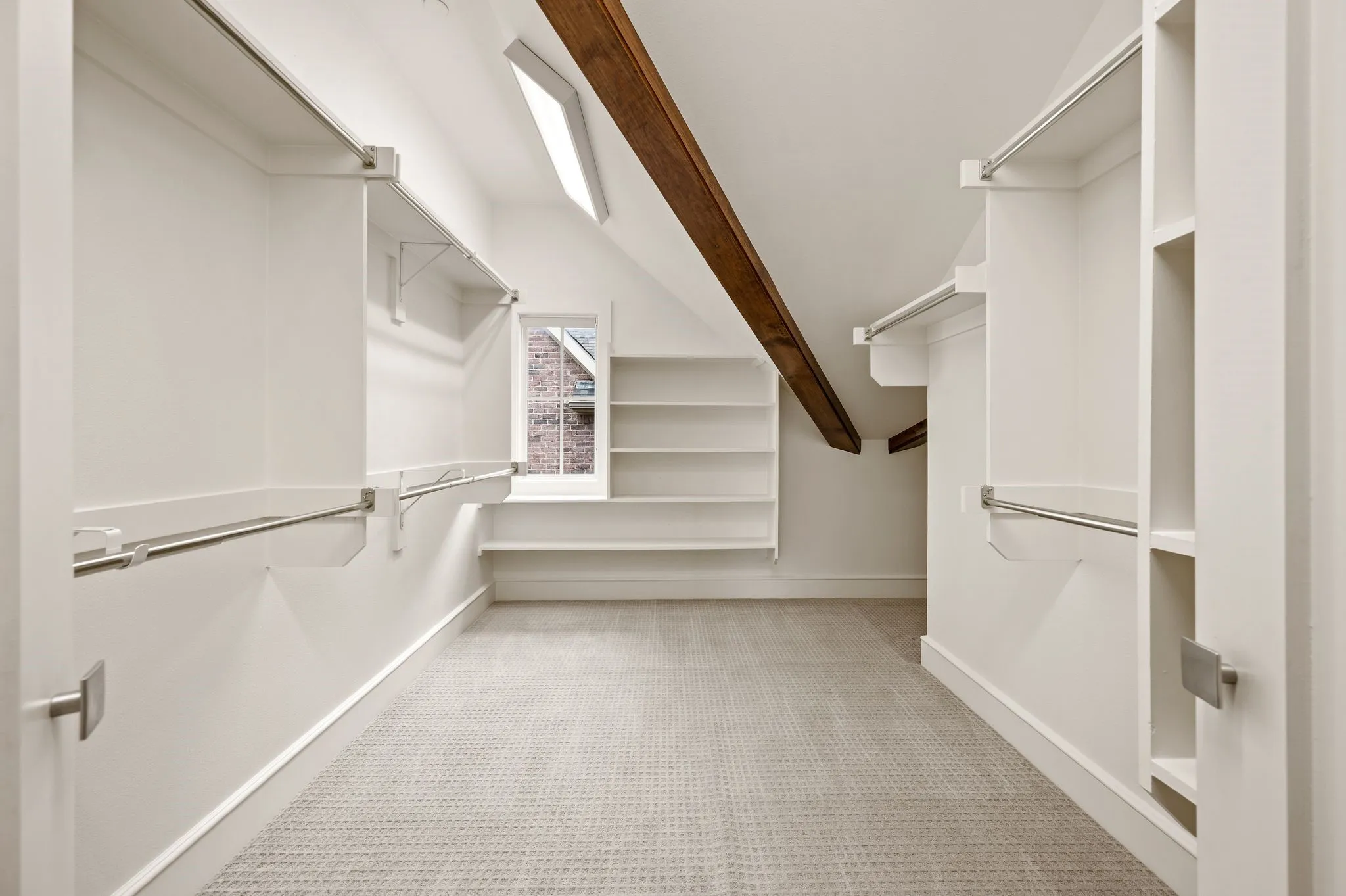 Expansive walk-in closet featuring white built-in shelving, chrome hanging rods, a textured carpet floor, and overhead fluorescent lighting