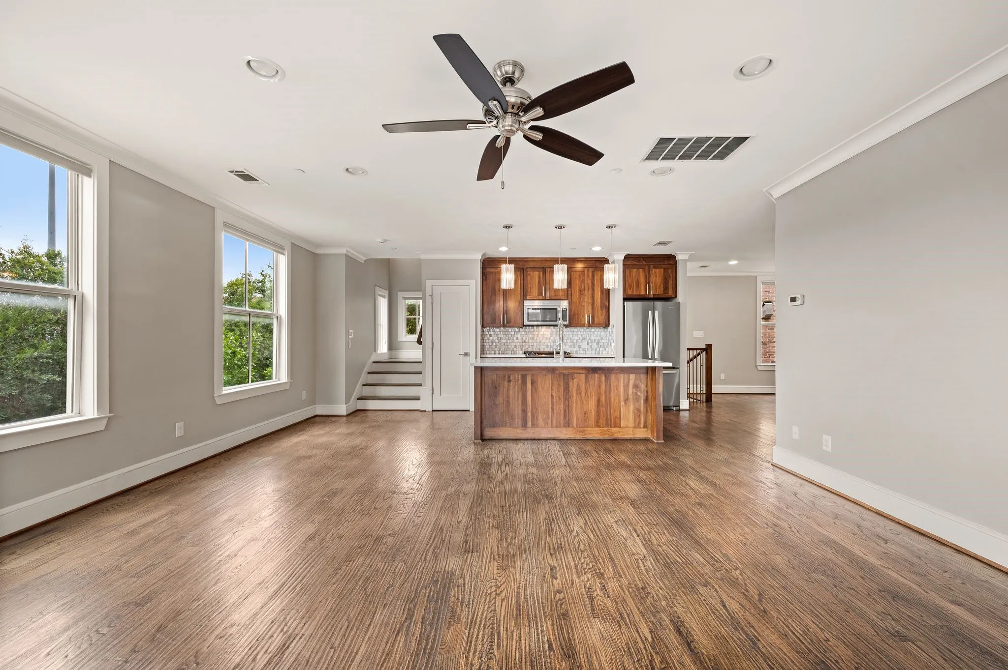 Open-concept living area featuring rich wood-finish flooring, a contemporary ceiling fan, recessed lighting, and a modern kitchen island with pendant lighting