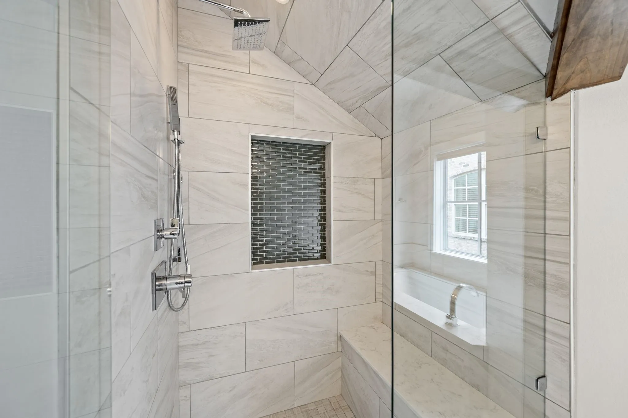 Glass-enclosed shower featuring white large-format tile, a built-in bench, a recessed niche with mosaic tile, a rainfall showerhead, and a handheld shower fixture