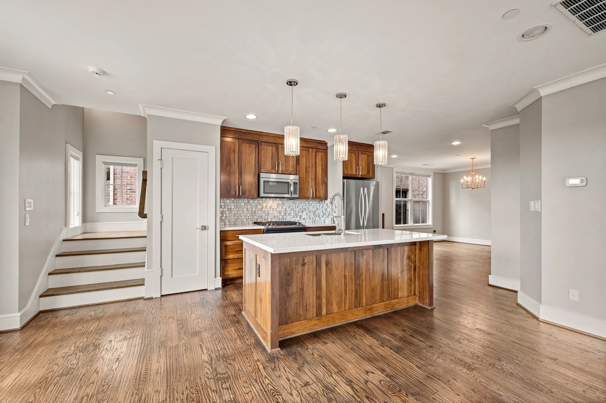 Kitchen with a central island featuring a white countertop and three pendant lights, wood-finish flooring, recessed lighting, and stainless steel appliances
