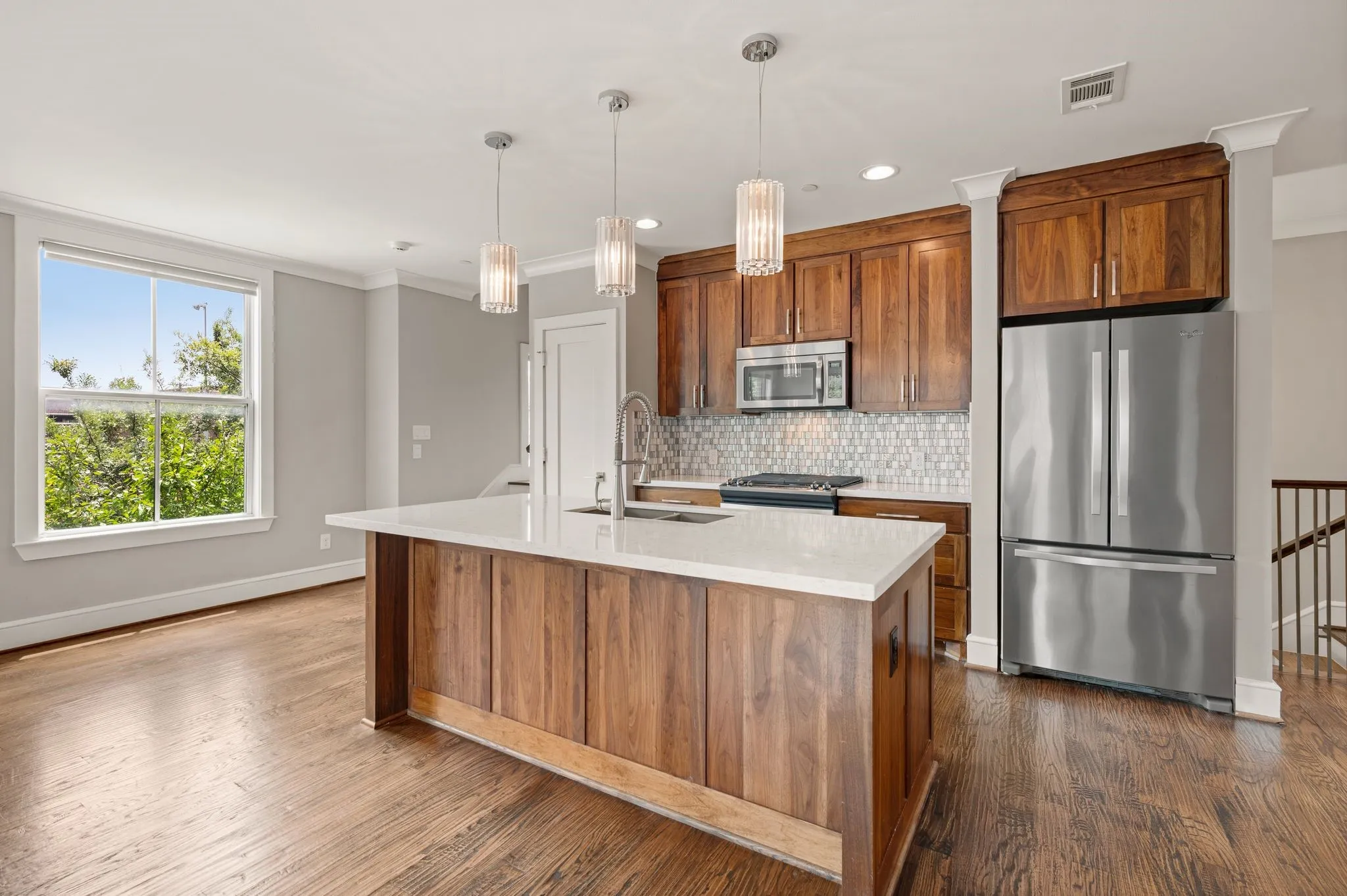 Open-concept kitchen featuring a large island with white countertop, rich wood cabinetry, stainless steel appliances, a mosaic tile backsplash, and wood-finish flooring