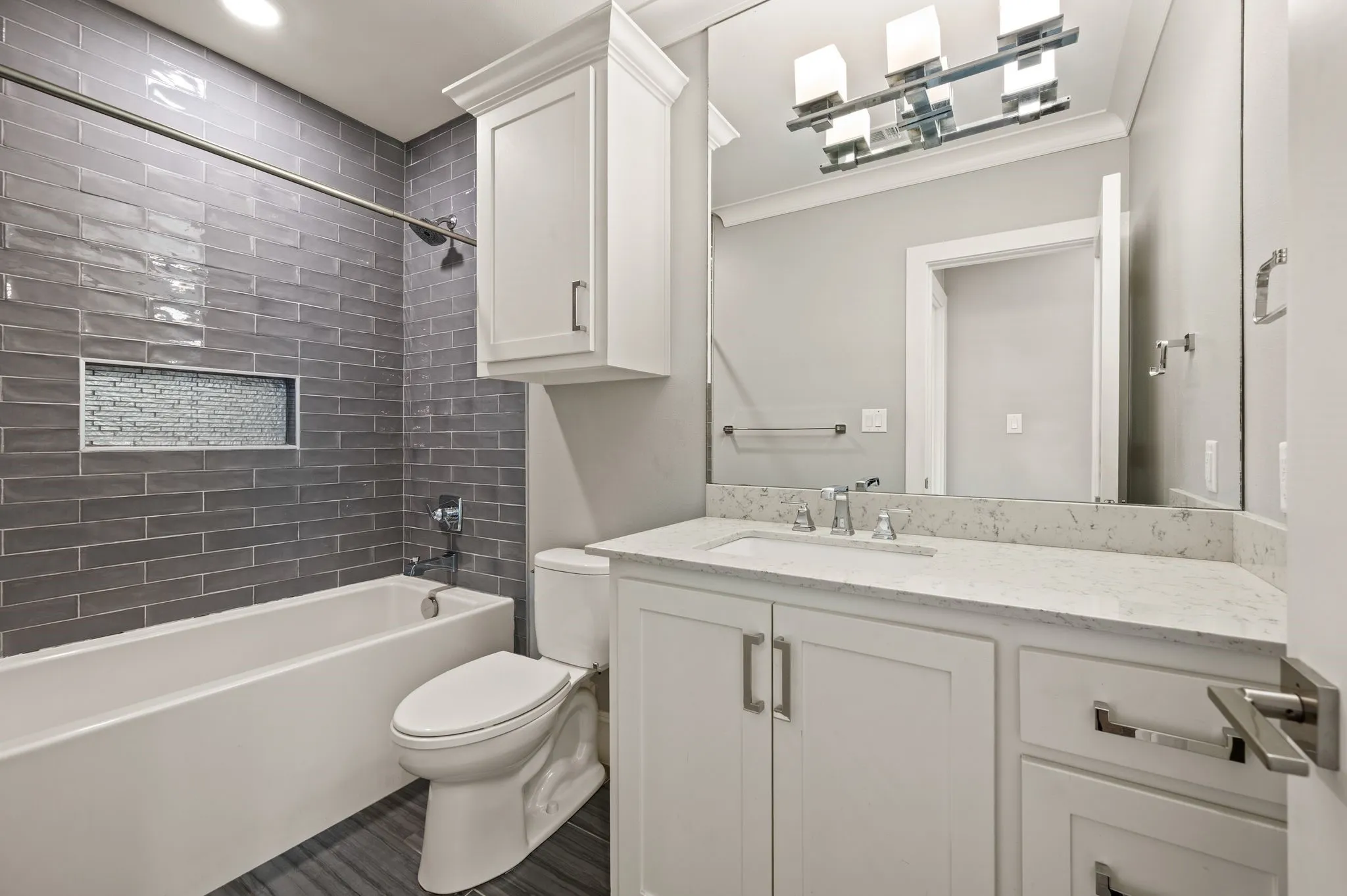 Bathroom featuring a white bathtub with dark gray subway tile surround and mosaic-tiled niche