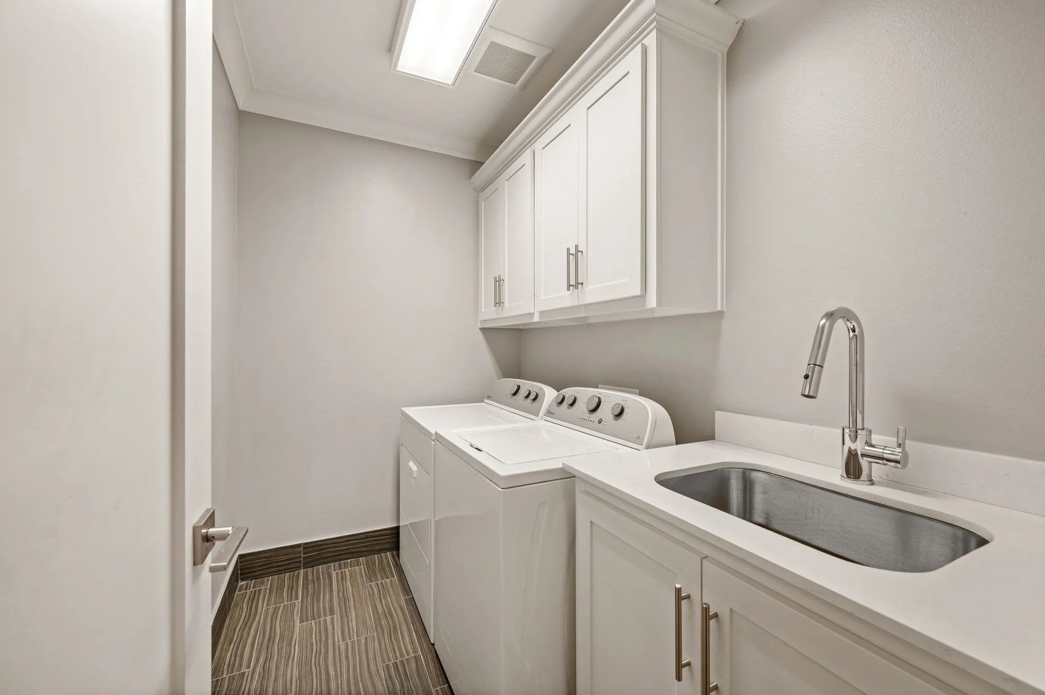 Laundry area featuring white cabinetry, a built-in stainless steel sink, a pull-down chrome faucet, light-toned countertops, and wood-finish flooring