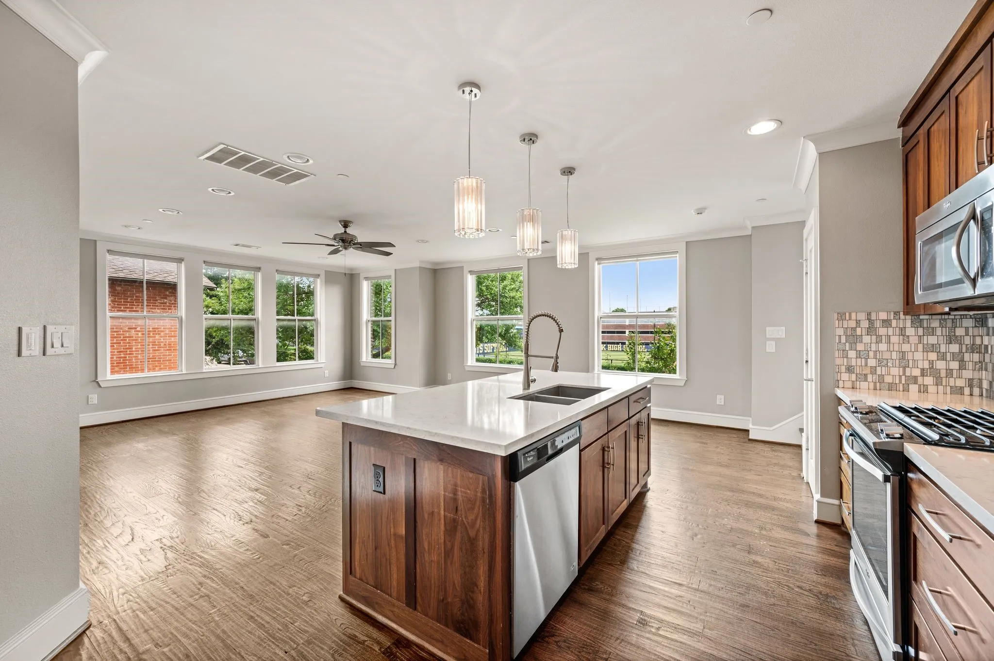Open-concept living space featuring wood-finish flooring, a contemporary kitchen island with a built-in sink and stainless steel dishwasher, and pendant lighting