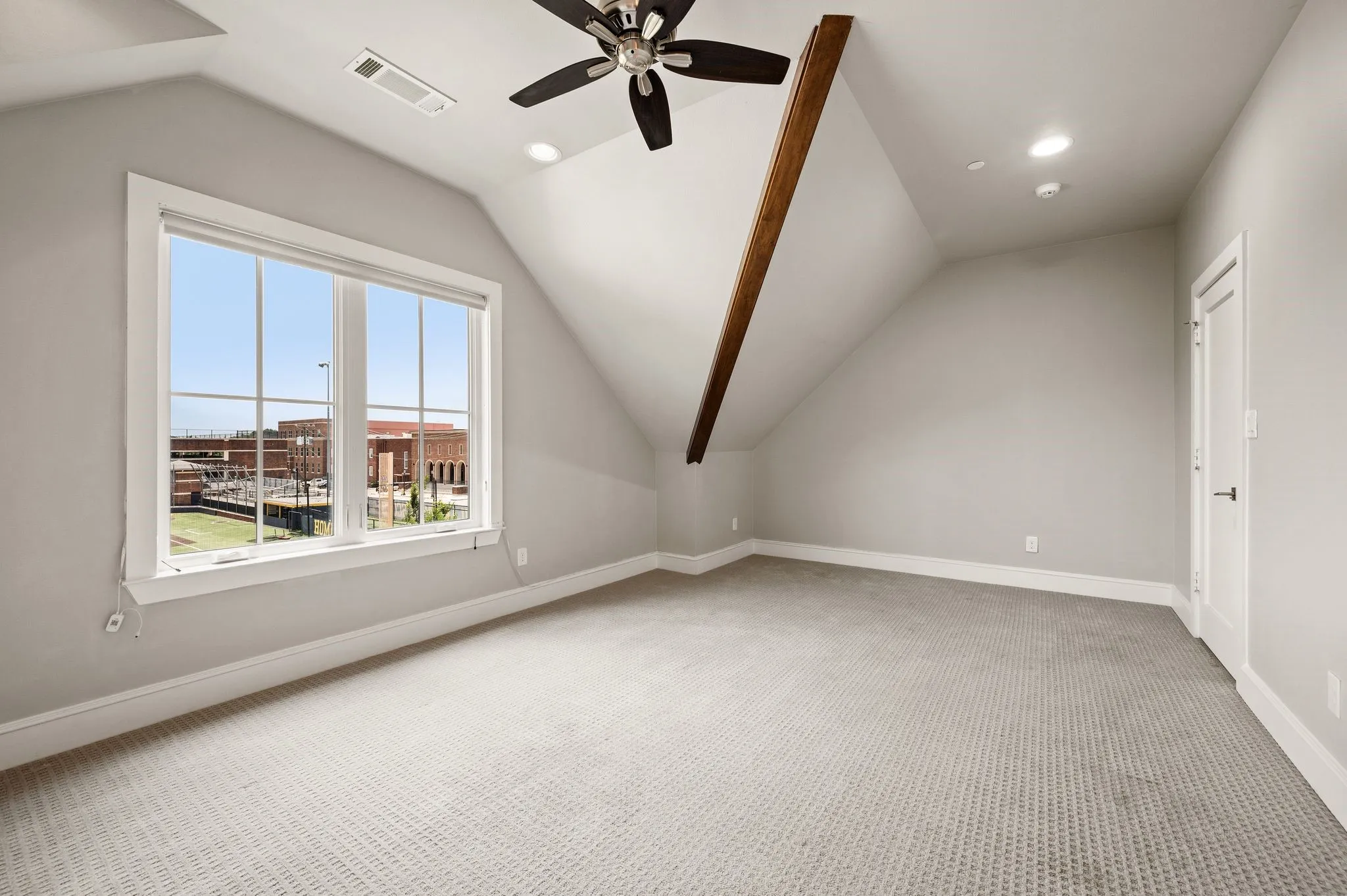 Carpeted room with a large window, sloped ceilings, and a dark wood beam accent
