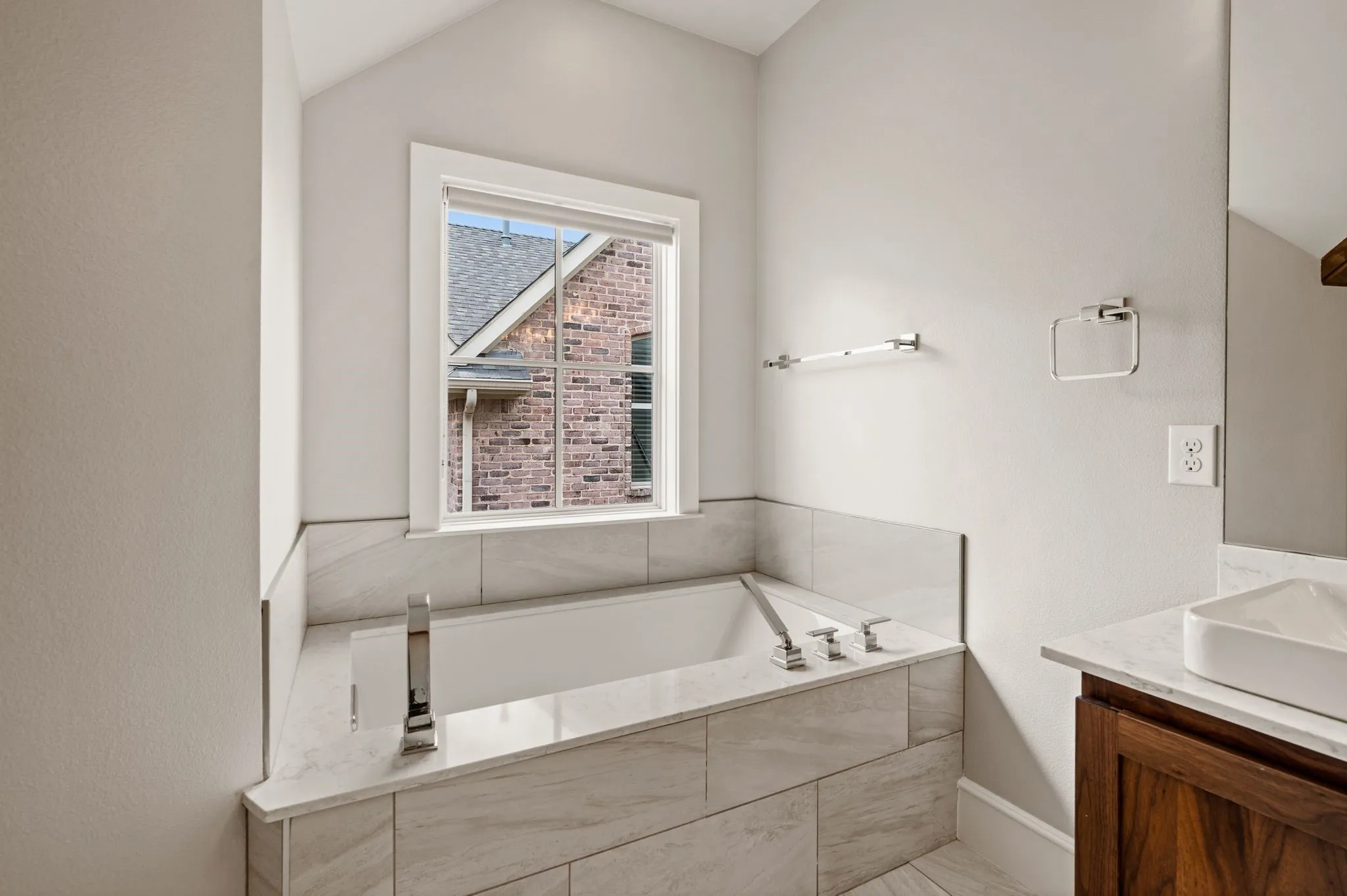 Soaking tub with chrome fixtures, surrounded by large format tile with a light stone-finish