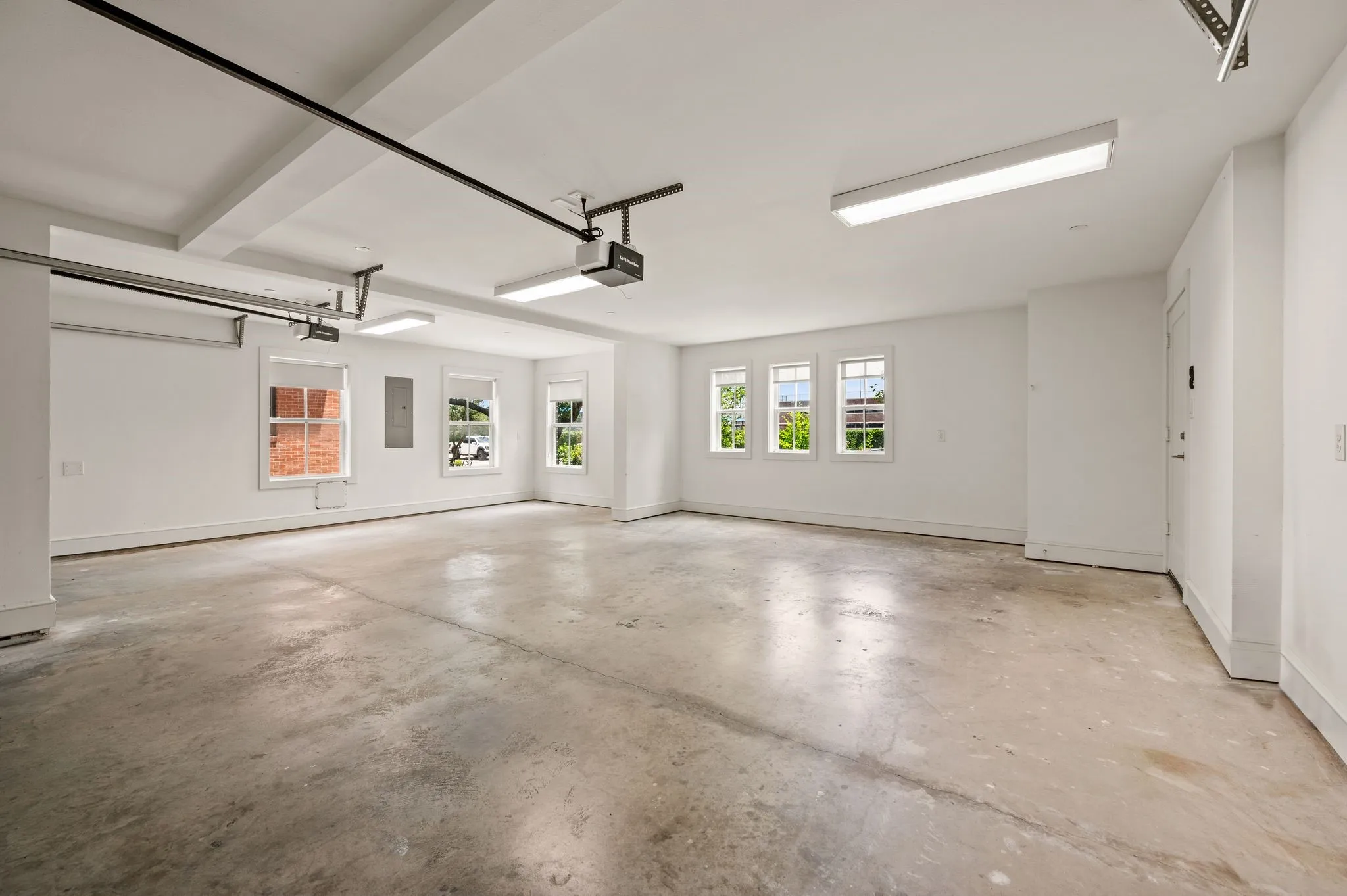 Spacious garage featuring a concrete floor, multiple windows, bright overhead lighting, a garage door opener system, and white painted walls