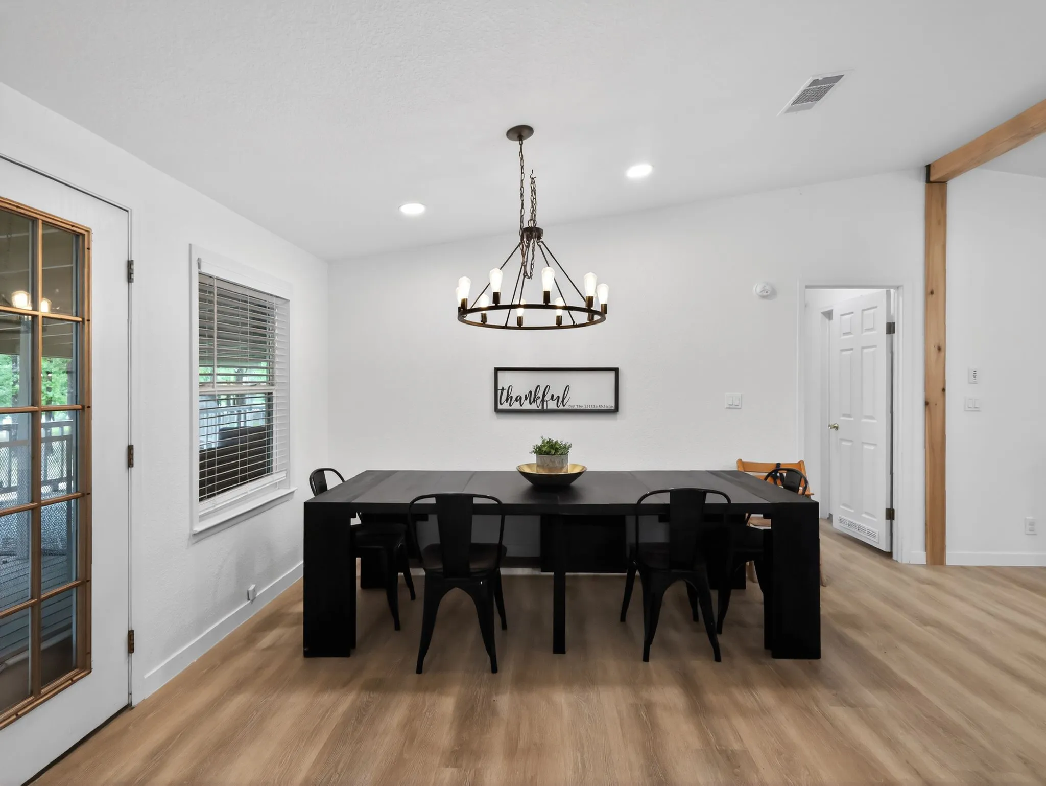 Spacious dining area featuring wood-finish flooring, a contemporary chandelier, a window with blinds, and a glass-paneled door