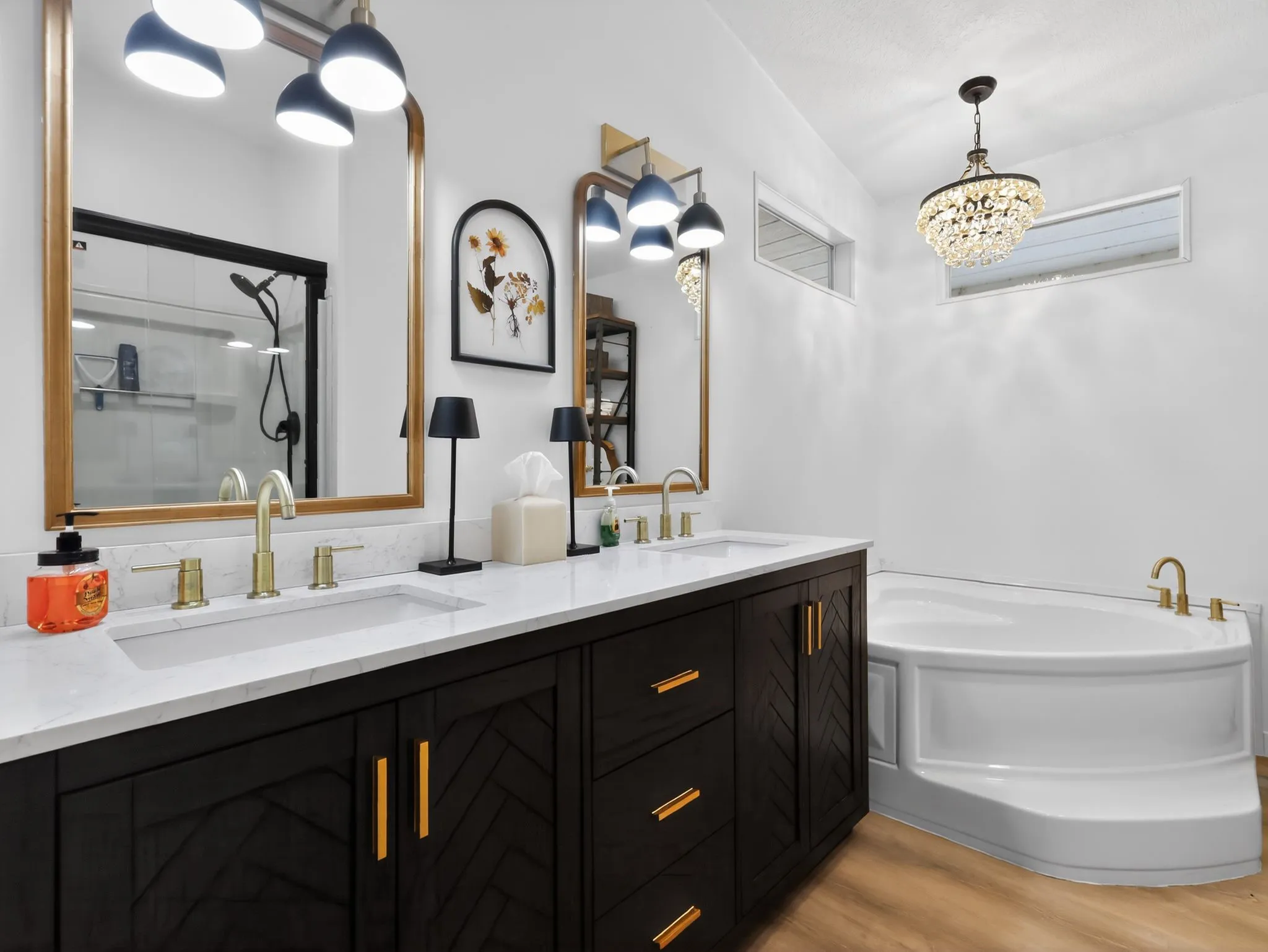 Double vanity with a white countertop and gold-finish fixtures, a corner soaking tub, a shower enclosure with black-finish hardware, and wood-finish flooring