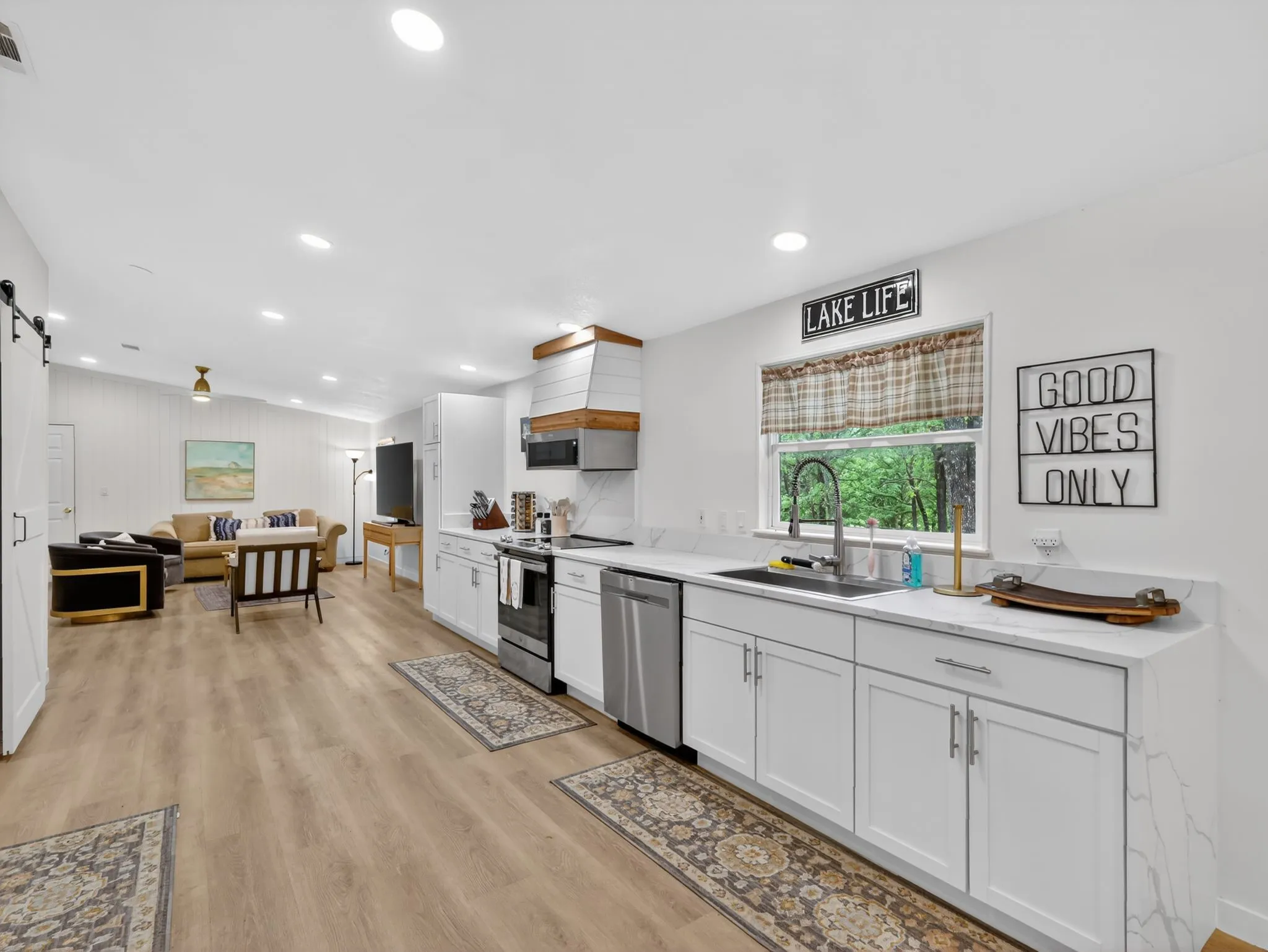 Kitchen featuring white cabinetry, light-toned countertops, a stainless steel sink with a gooseneck faucet, a built-in microwave, and wood-finish flooring