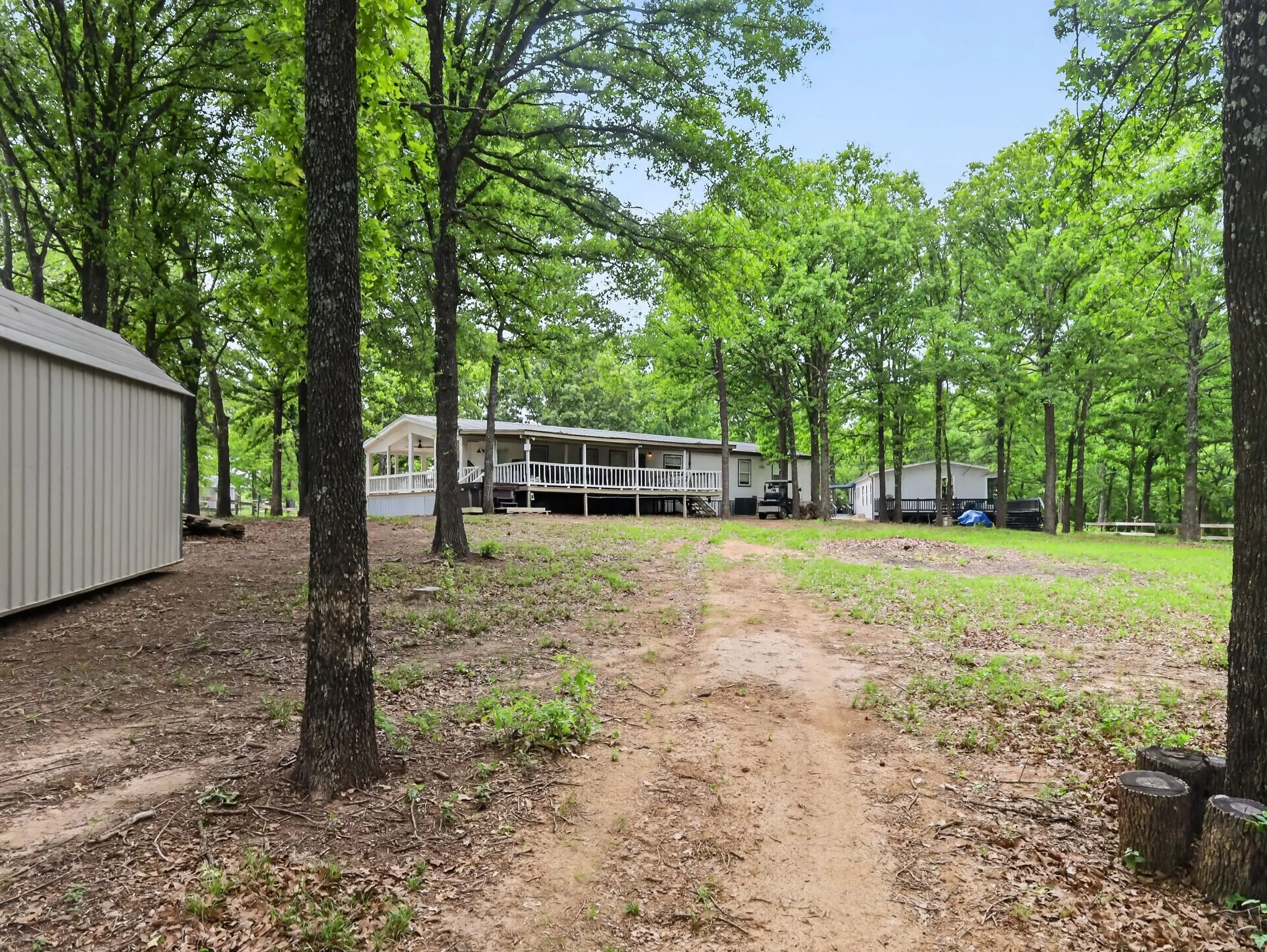 Expansive property featuring a single-story residence with a full-length covered porch, surrounded by mature trees