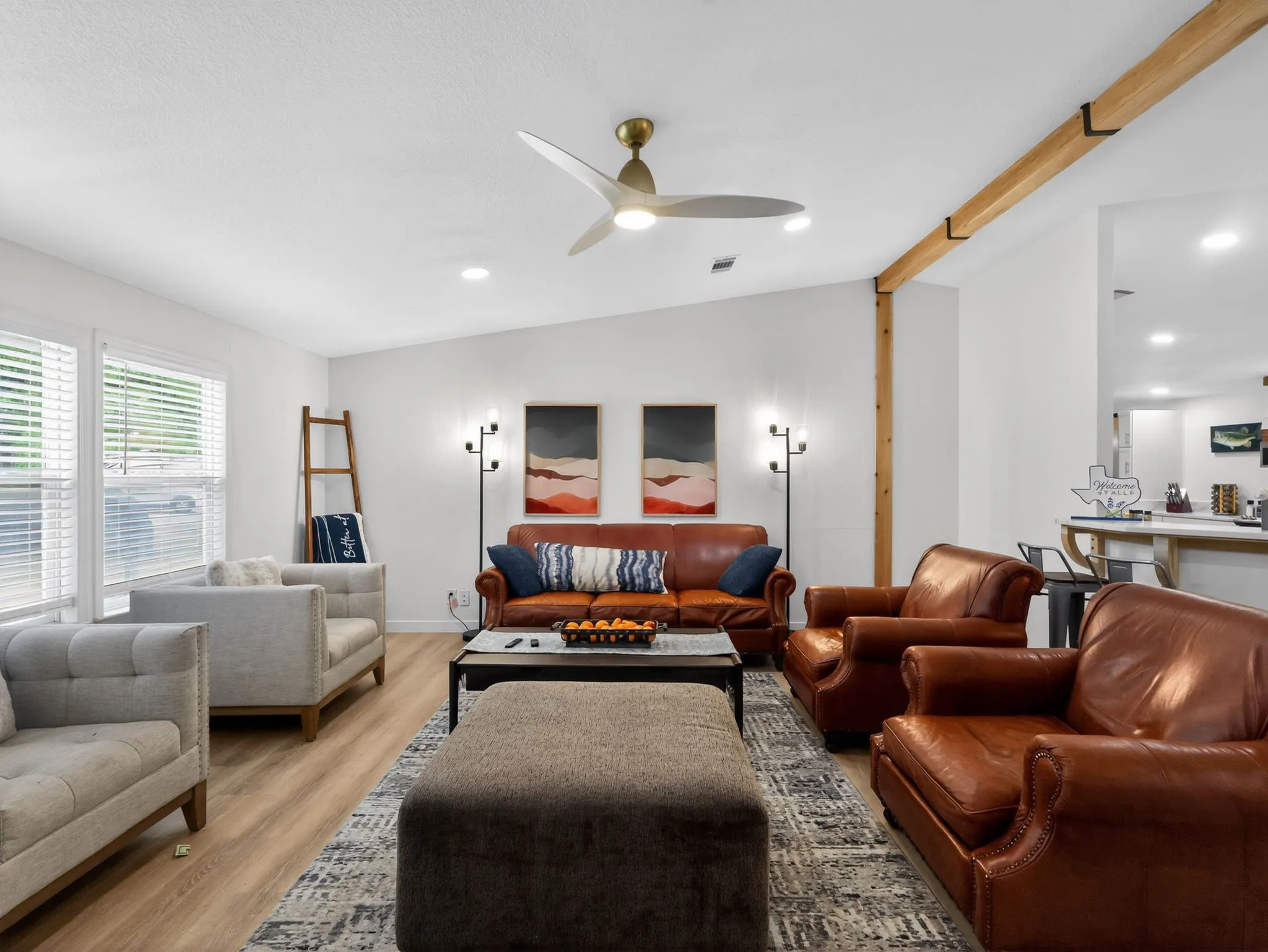 Spacious living area featuring wood-finish flooring, a contemporary ceiling fan, recessed lighting, white walls, and prominent wooden beam accents