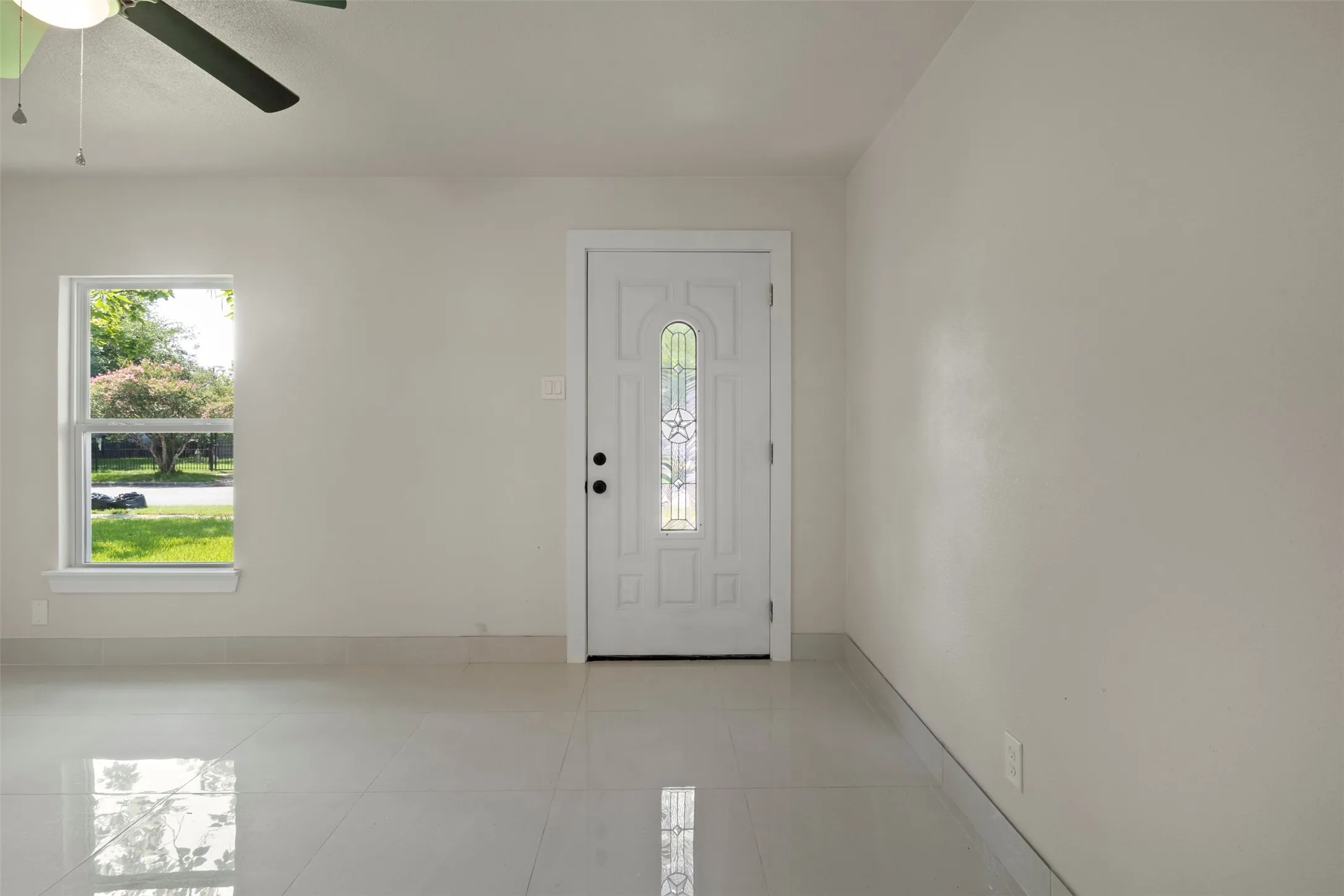 Entryway featuring a white door with decorative glass inserts, a single-pane window, light-colored walls, and glossy tile flooring