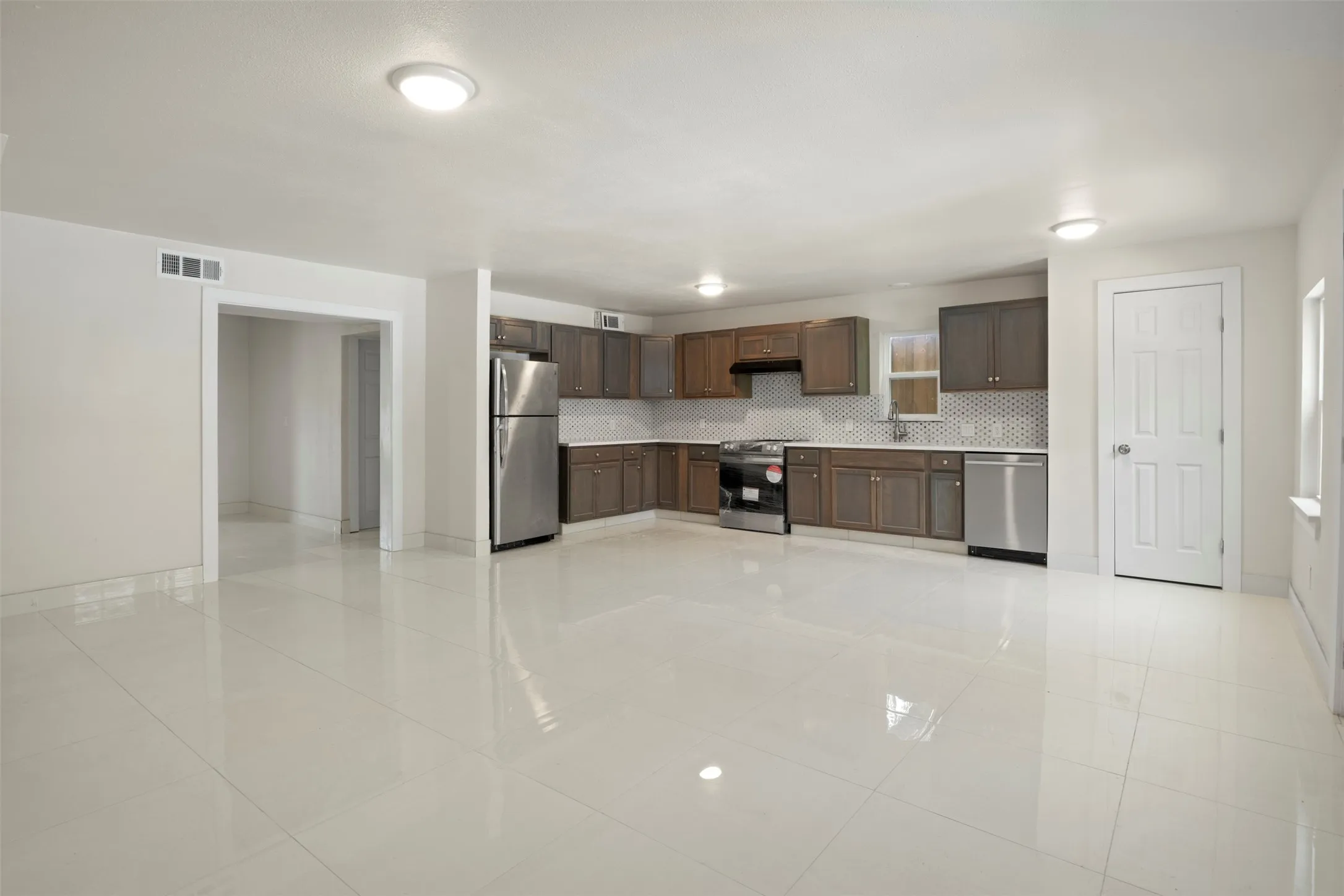 Spacious kitchen featuring stainless steel appliances, dark wood cabinetry, white countertops, and a patterned tile backsplash