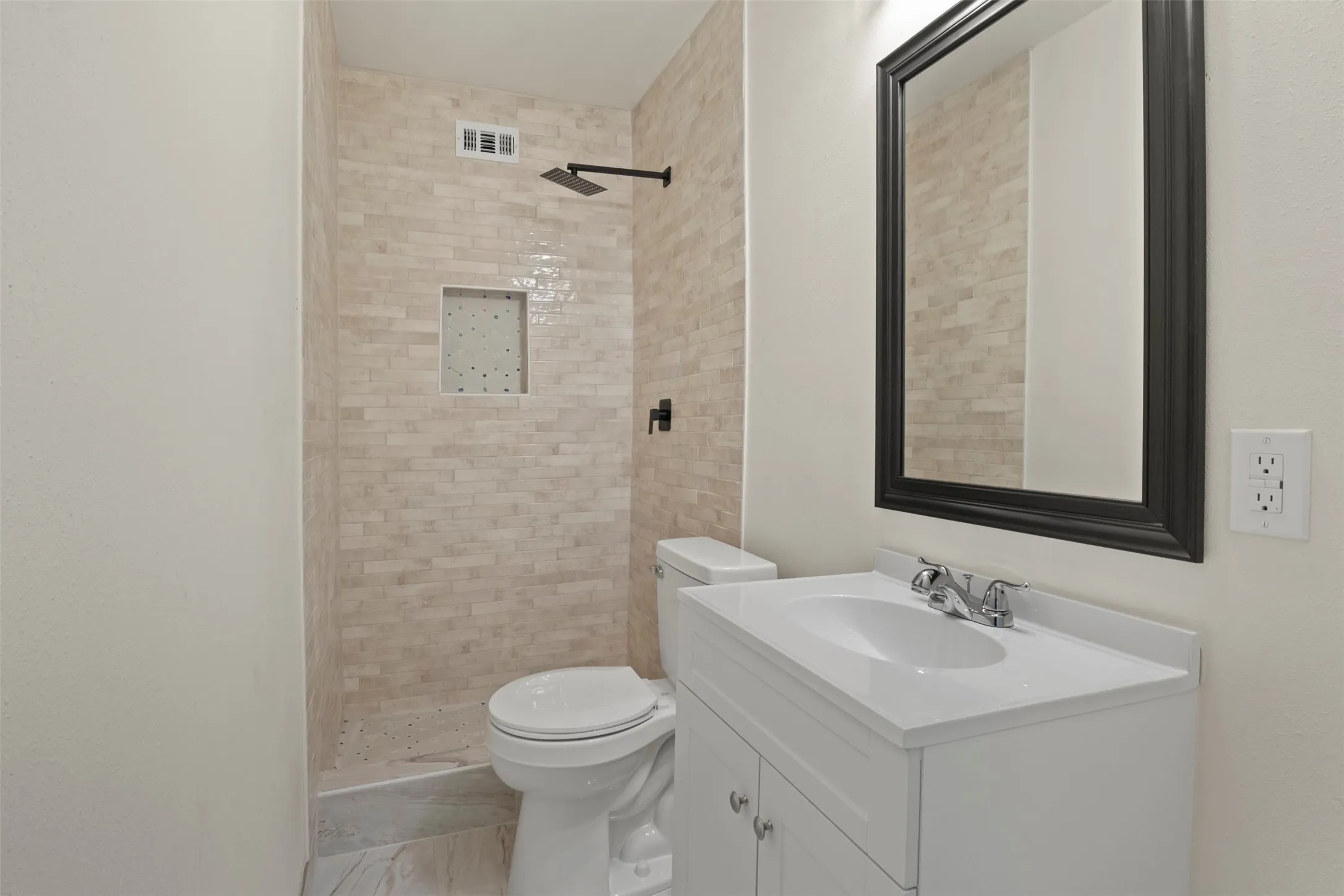 ensuite Bathroom in large bedroom upstairs featuring a shower with light-toned rectangular tile, a built-in shower niche, and a matte black rainfall showerhead