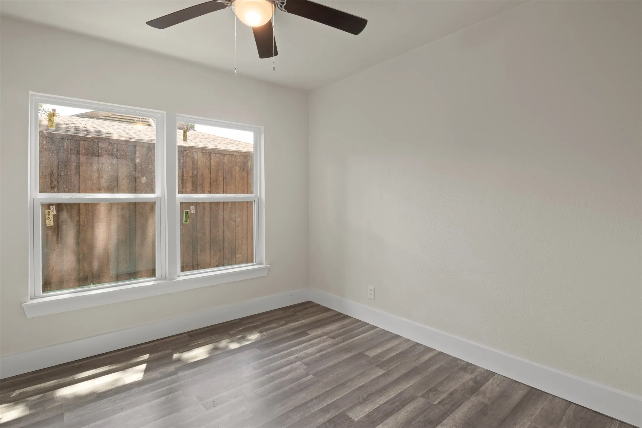 Bright room featuring two windows, wood-finish flooring, a ceiling fan with integrated lighting, and white baseboards