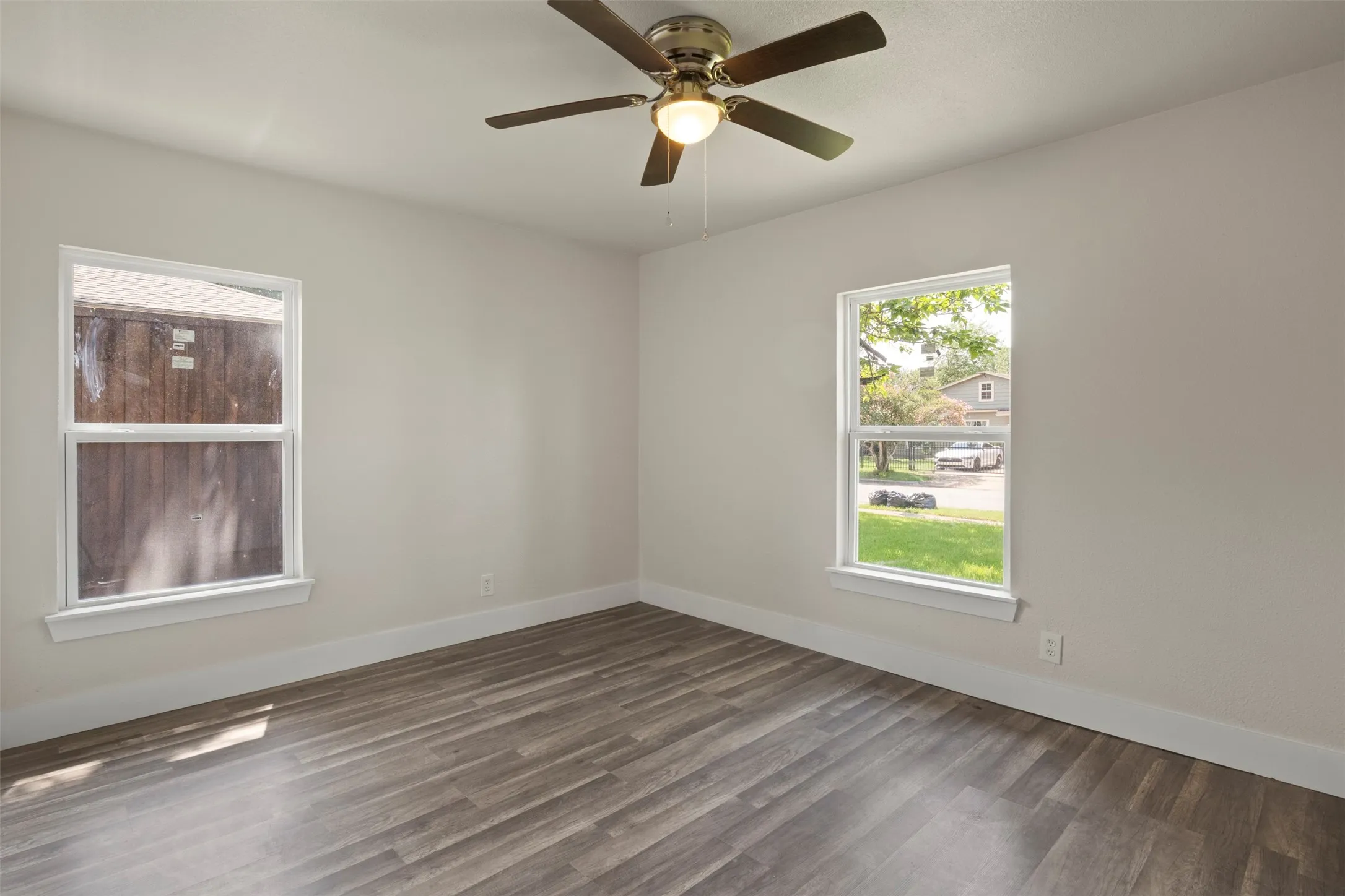Open room featuring wood-finish flooring, two windows with white trim, and a ceiling fan with integrated lighting