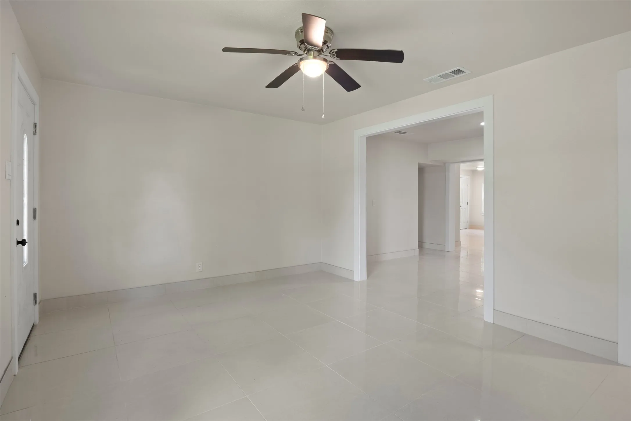 Expansive living area featuring light-toned tile flooring, neutral wall paint, and a ceiling fan with integrated lighting