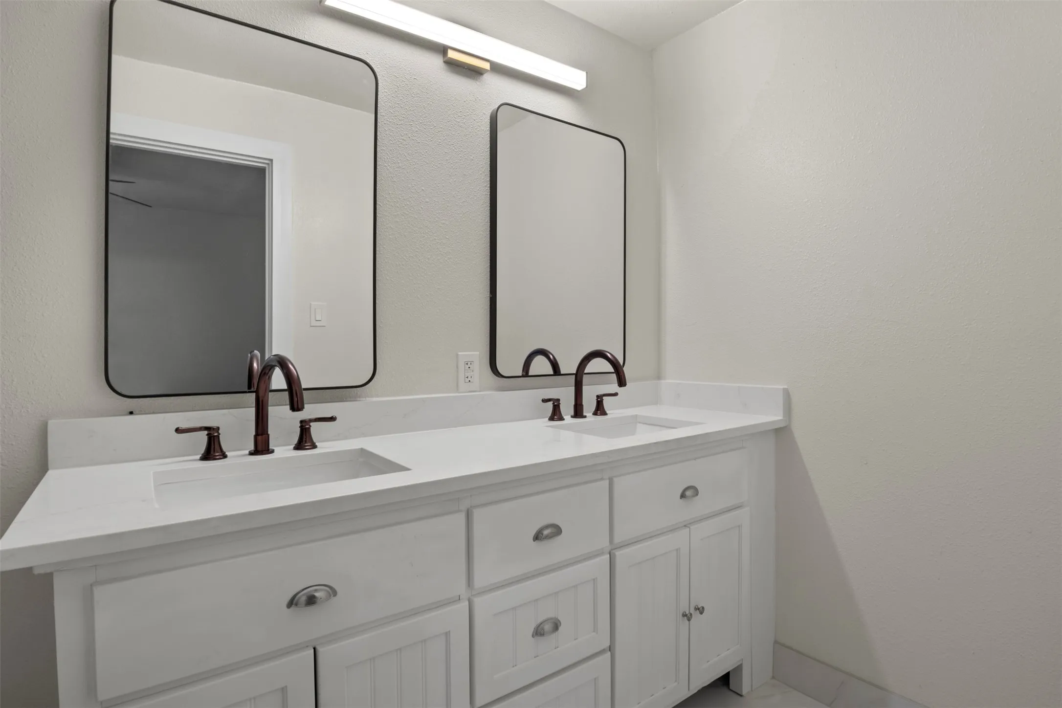 Double vanity featuring white cabinetry, integrated sinks, white countertops, and oil-rubbed bronze hardware