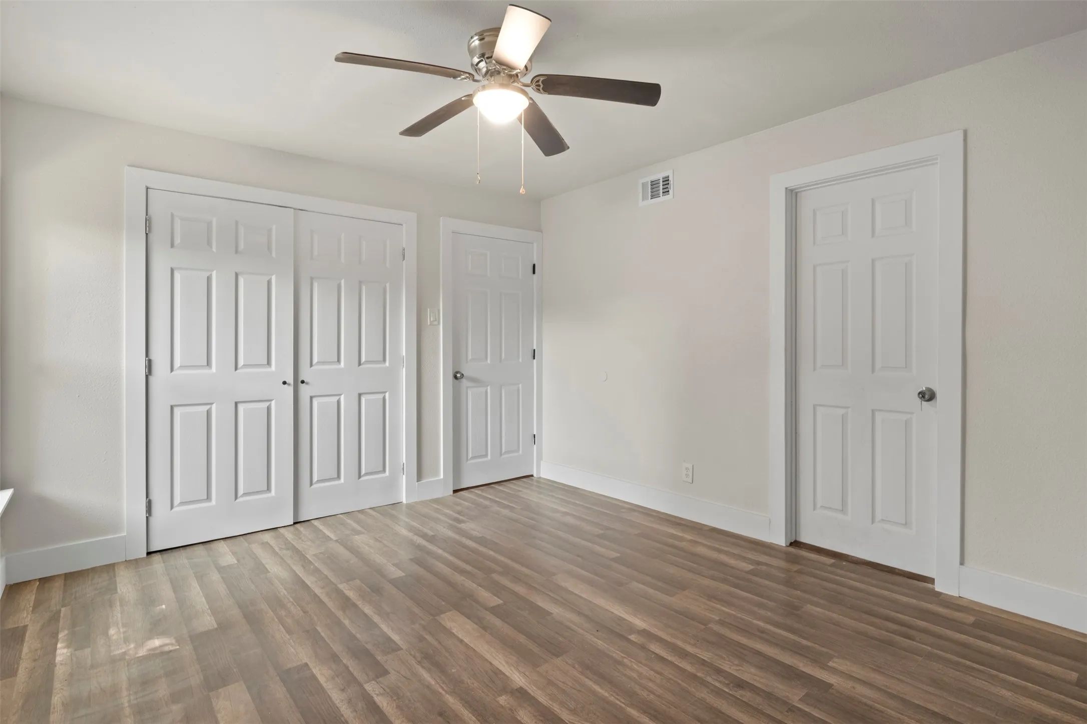 Bright room featuring wood-finish flooring, a ceiling fan with integrated lighting, and white baseboards