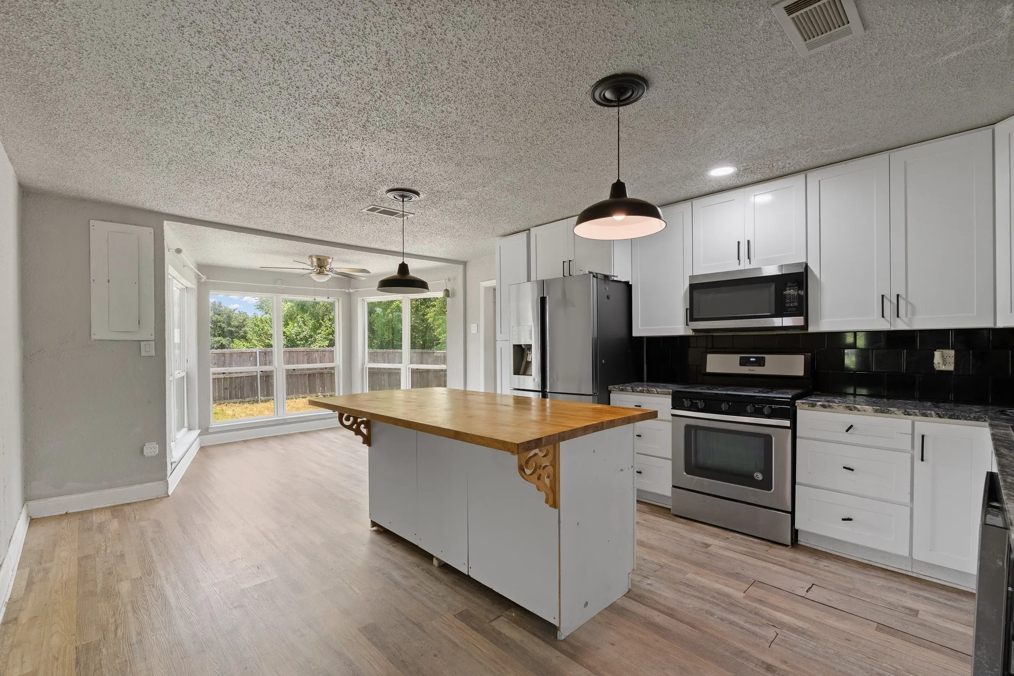 Kitchen featuring a central island with wood countertop, white shaker-style cabinetry, stainless steel appliances, and a black subway tile backsplash