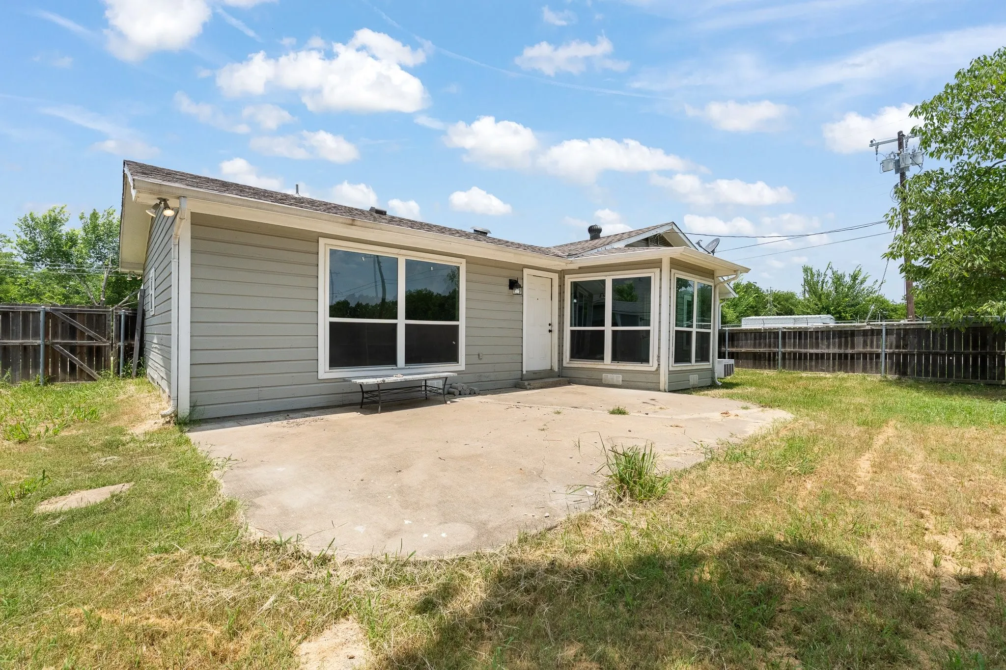 Rear exterior featuring light grey horizontal siding, multiple large windows, and a concrete patio