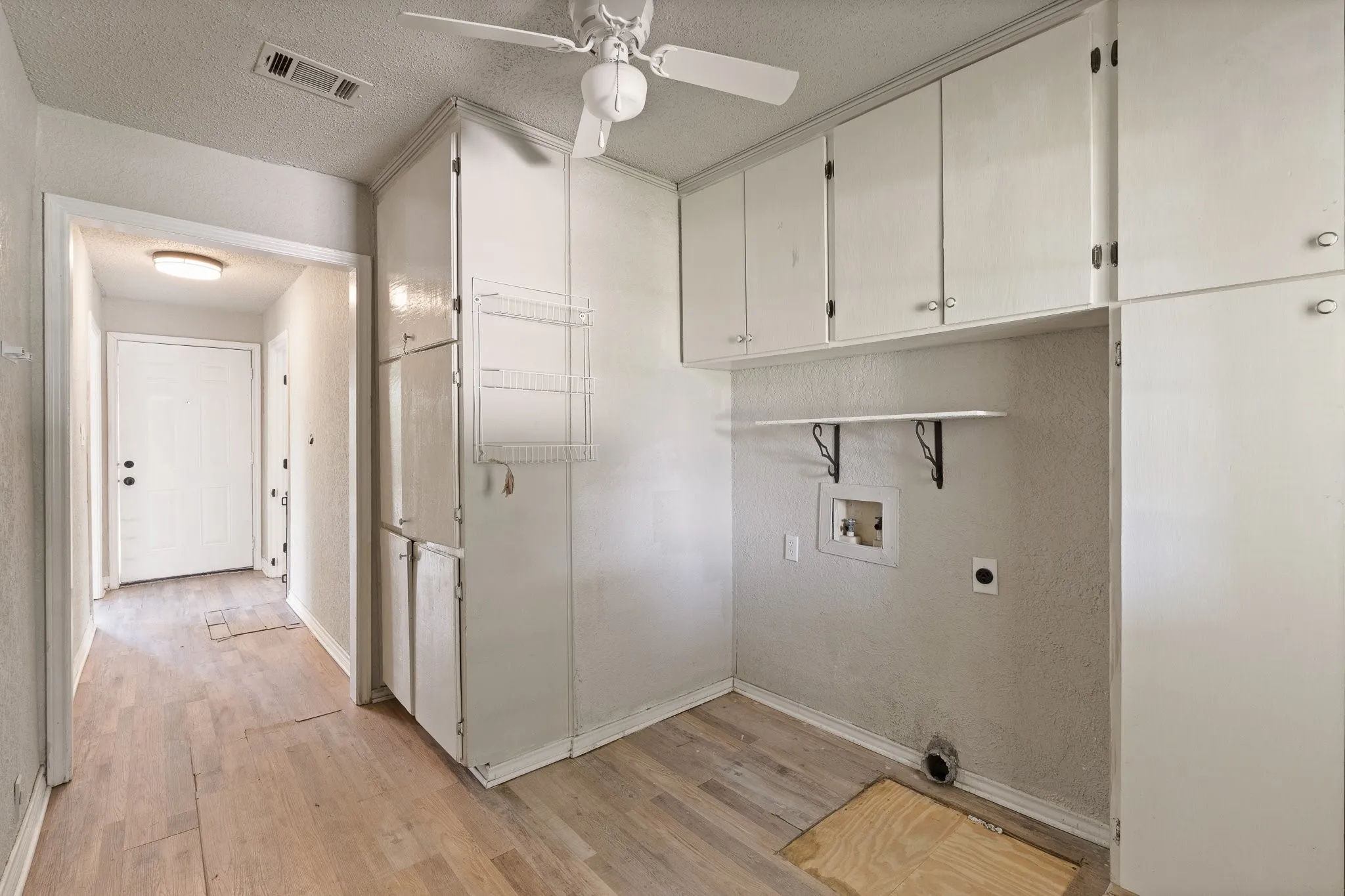 Utility area featuring abundant white cabinetry with silver-tone hardware, a ceiling fan, and wood-finish flooring