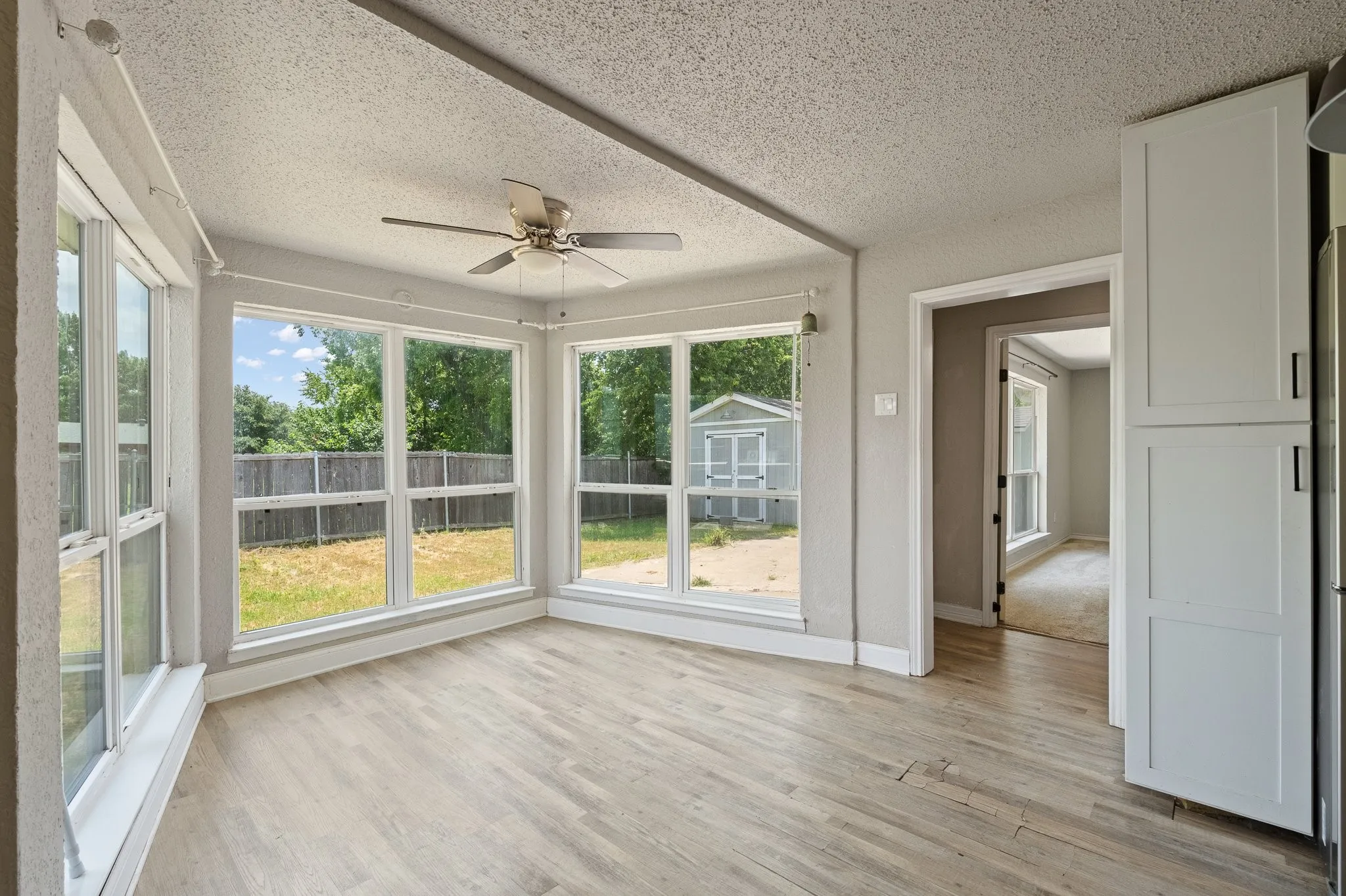 Sunroom featuring wood-finish flooring, a ceiling fan, and multiple large windows overlooking a fenced backyard with a storage shed