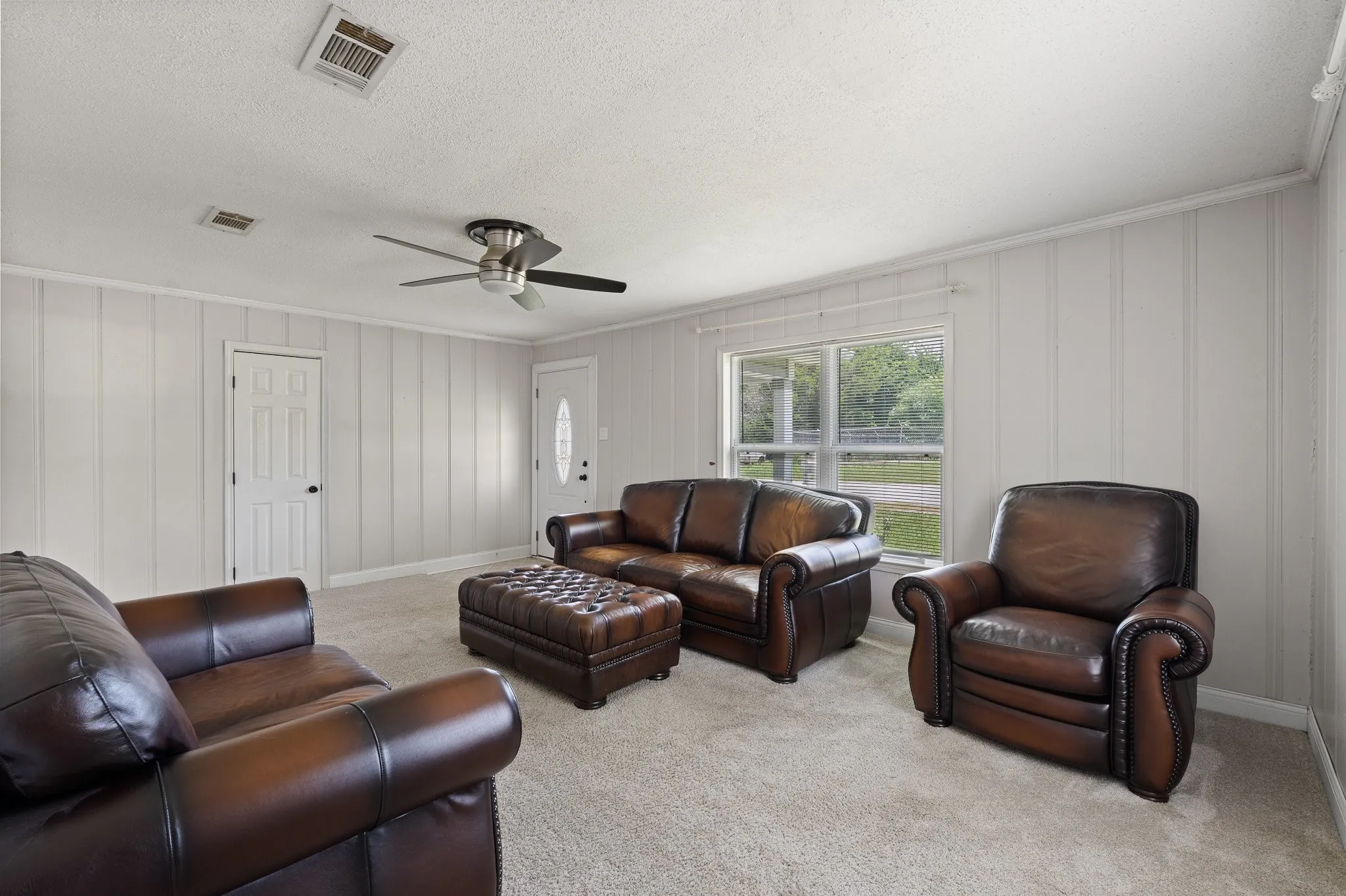 Carpeted living area featuring paneled walls and a ceiling fan