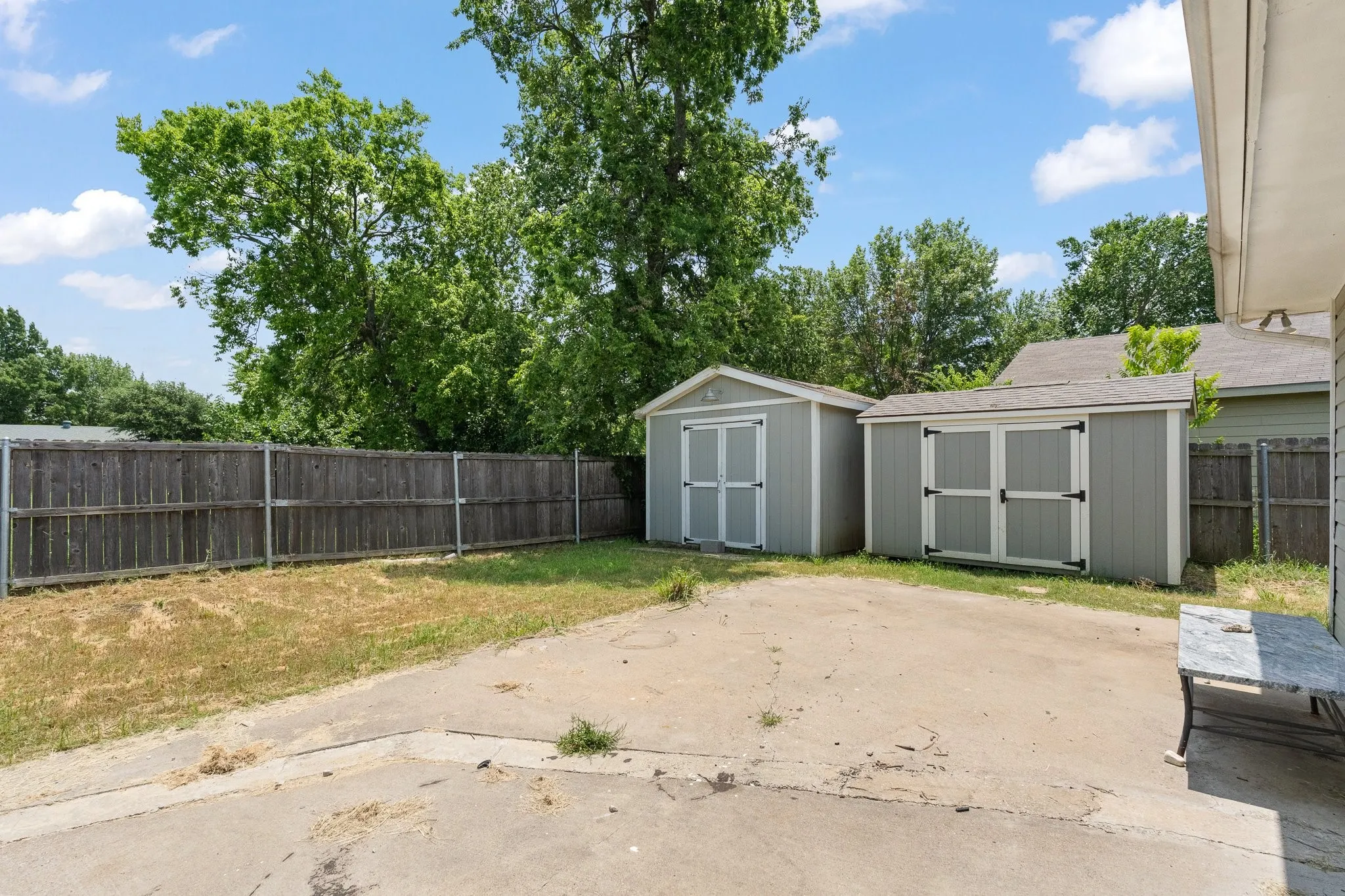 Outdoor space featuring two storage sheds, a concrete patio area, and a wood plank fence