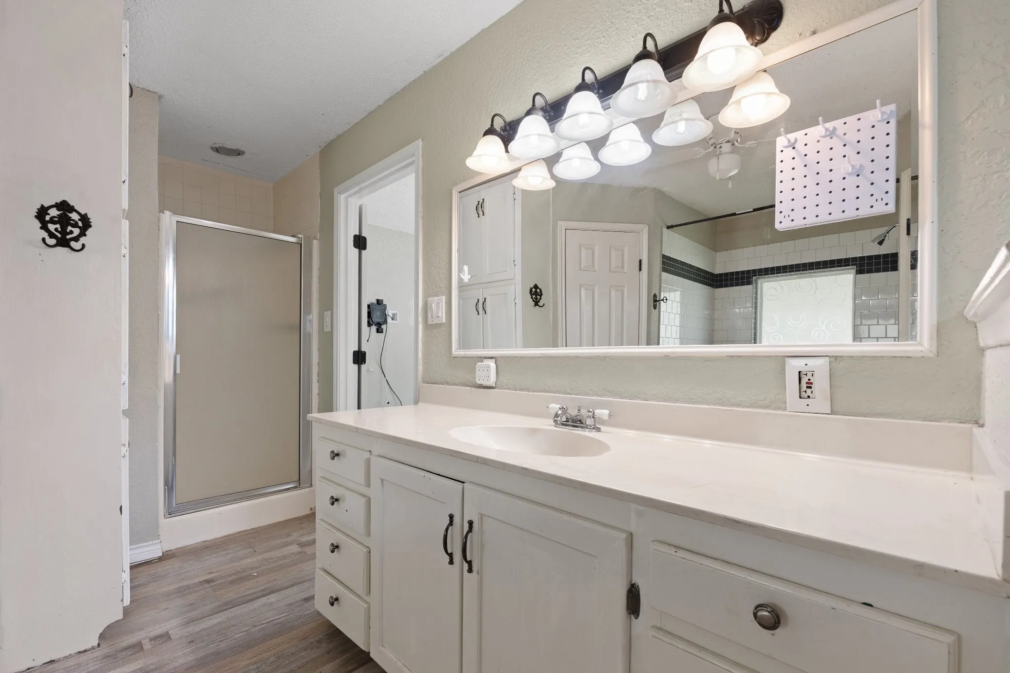 Bathroom featuring a spacious white vanity with ample storage, a single basin sink, and a large wall-mounted mirror with an eight-bulb light fixture