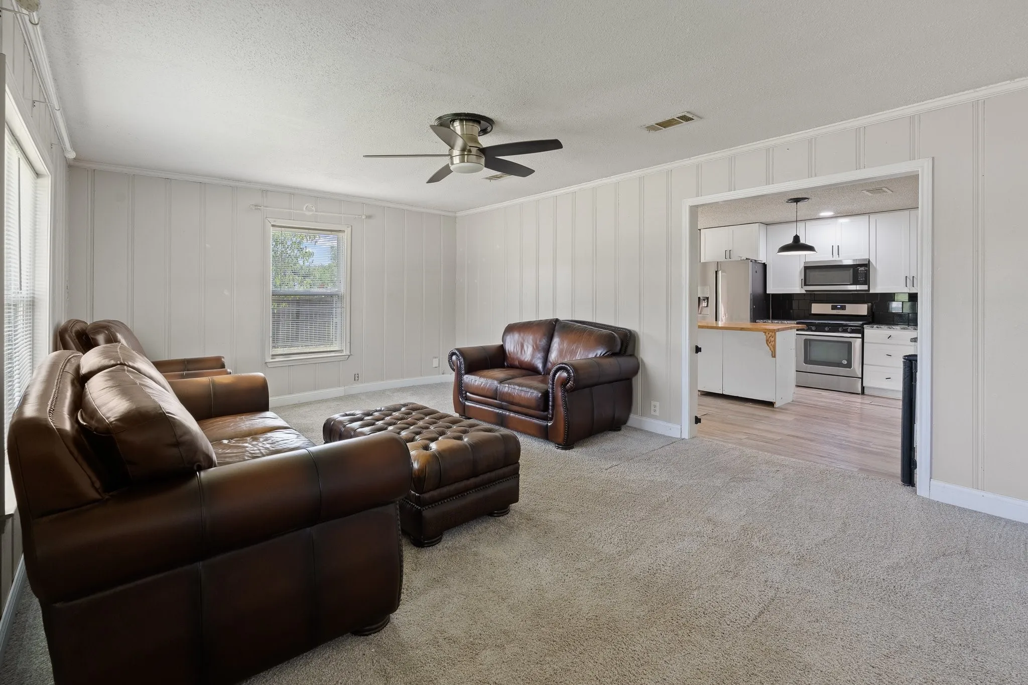 Living area with neutral carpeting and a ceiling fan, featuring board and batten wall details