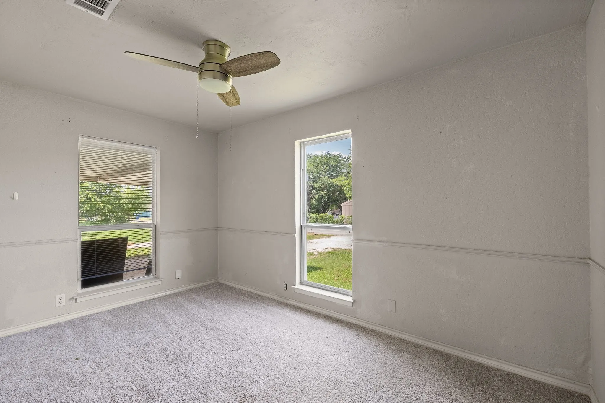 Carpeted room featuring two windows, a ceiling fan with integrated lighting, and a chair rail molding