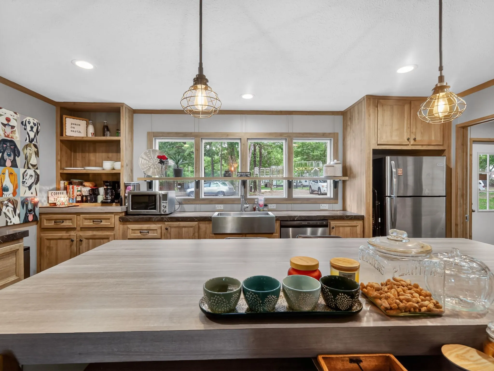Kitchen featuring a large central island, light wood-finish cabinetry, stainless steel appliances, and a farmhouse-style sink with a window outlook