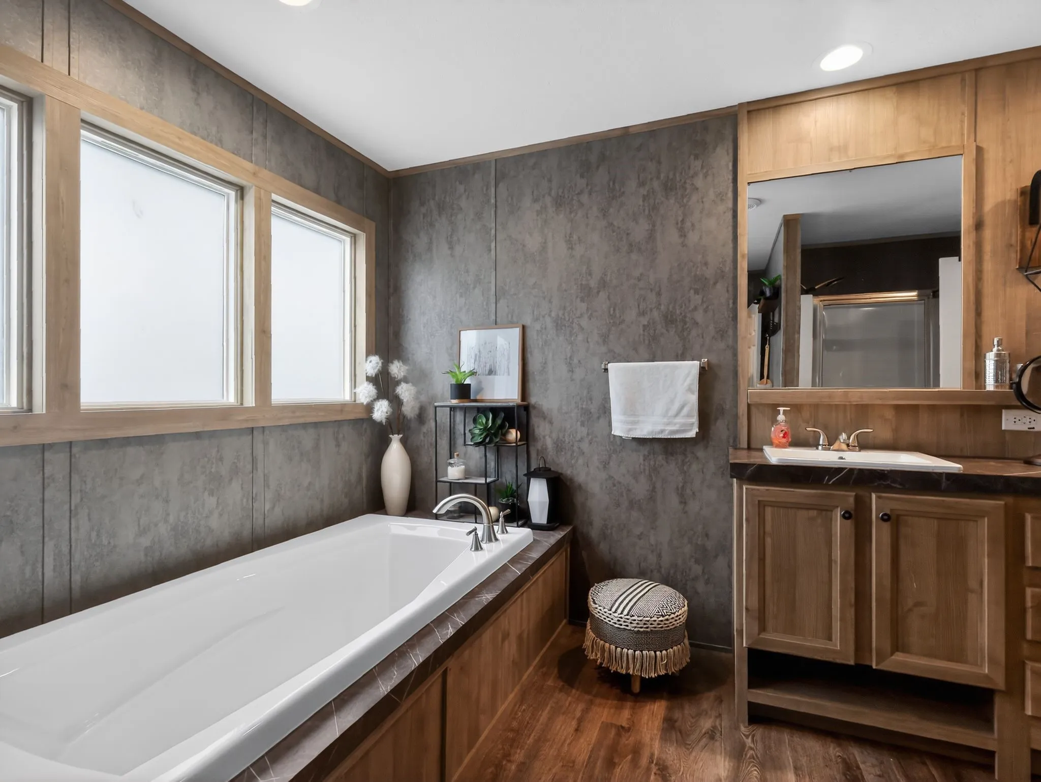 Bathroom featuring a built-in soaking tub with a wood-finish surround, a single vanity with a dark countertop and integrated sink, and wood-finish flooring